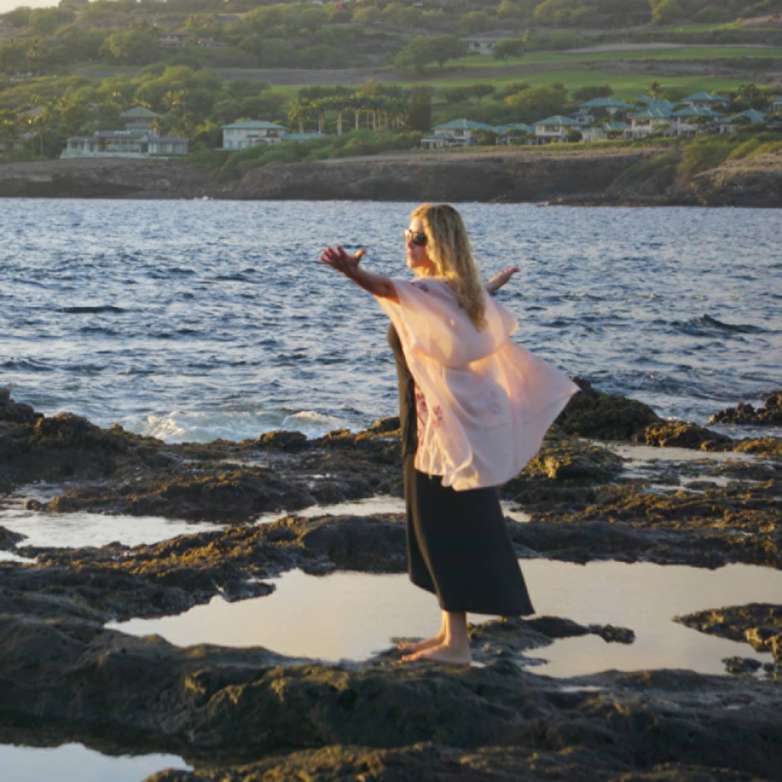 A woman meditates at edge of ocean on lava rock