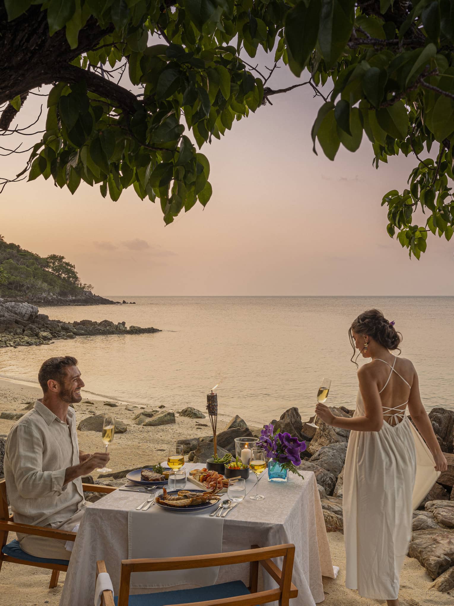 Couple enjoys romantic beachside dinner at sunset on the craggy shores