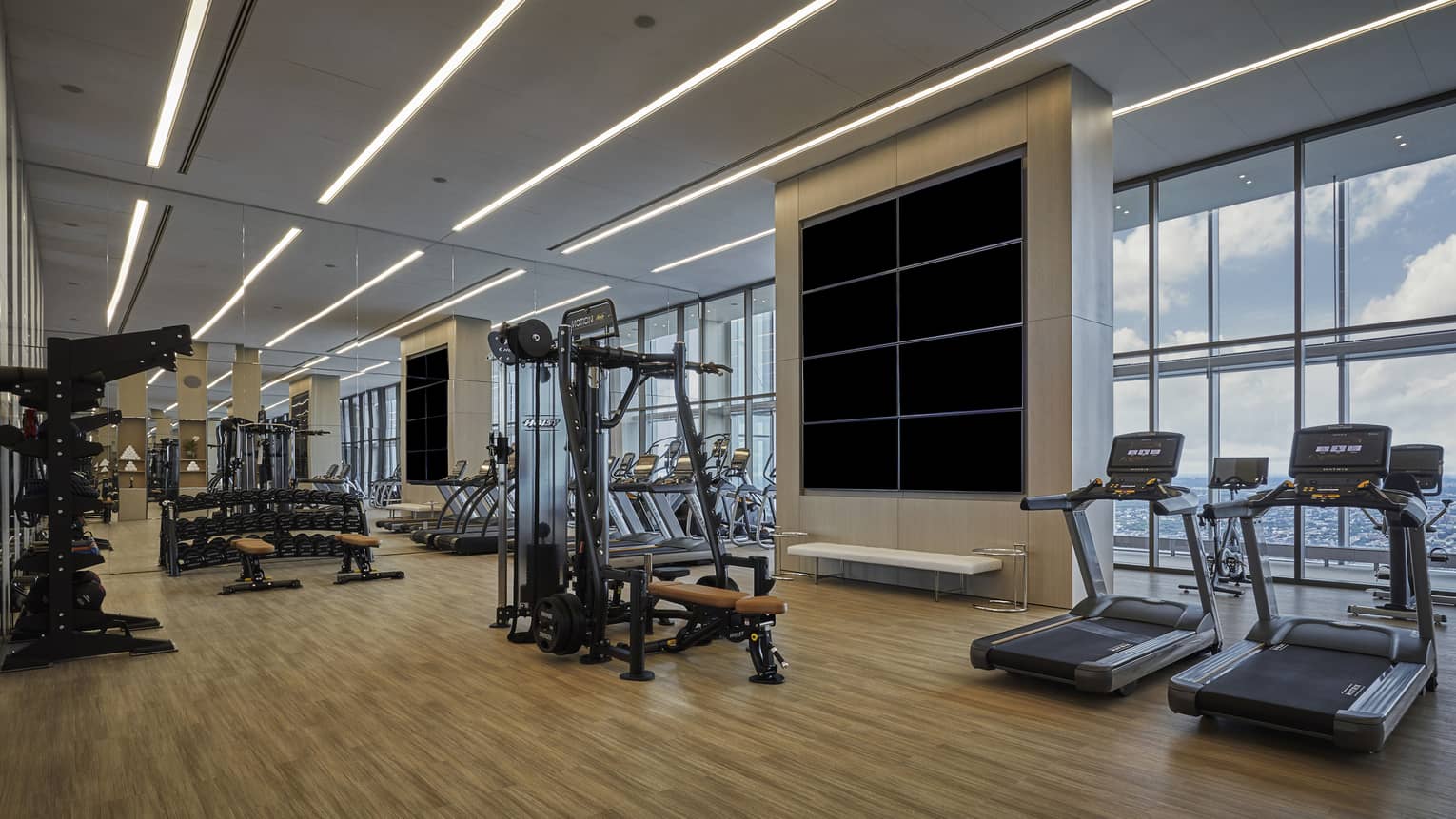 A spacious fitness center with large windows overlooking a city skyline