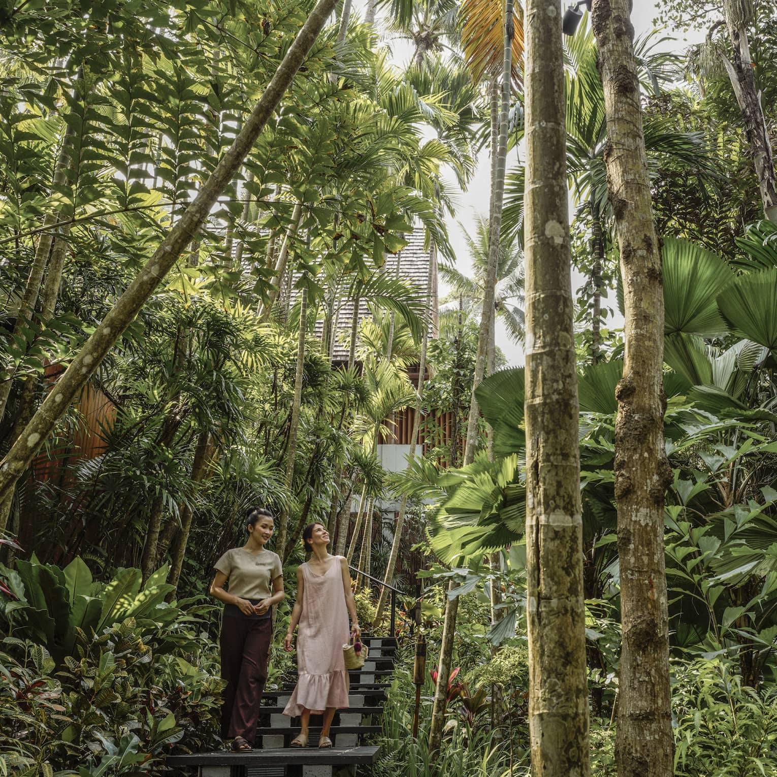 Female guest and spa staff member walk along foliage-lined pathway to the spa