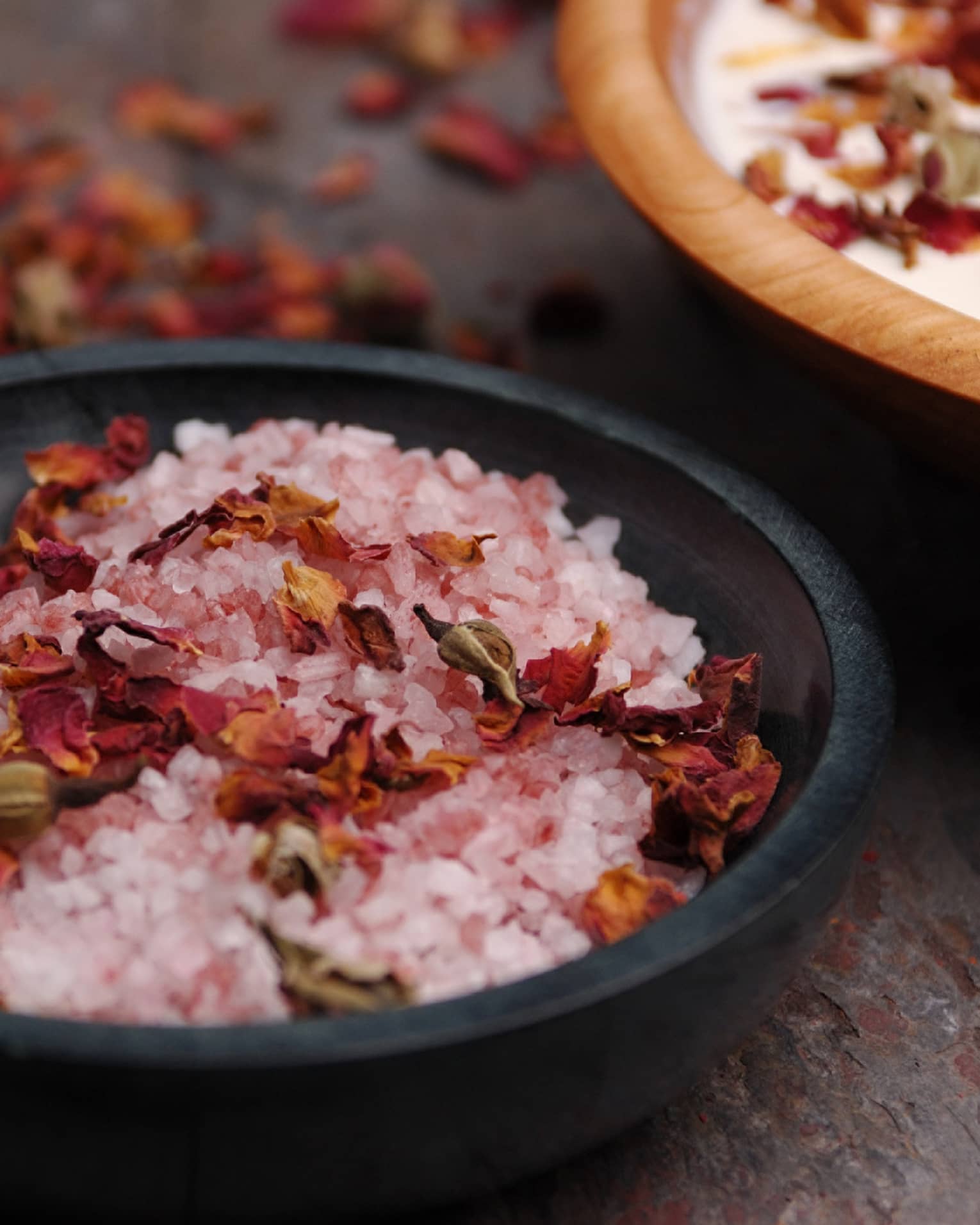 Pink crystals or salt and red flowers in a black bowl.