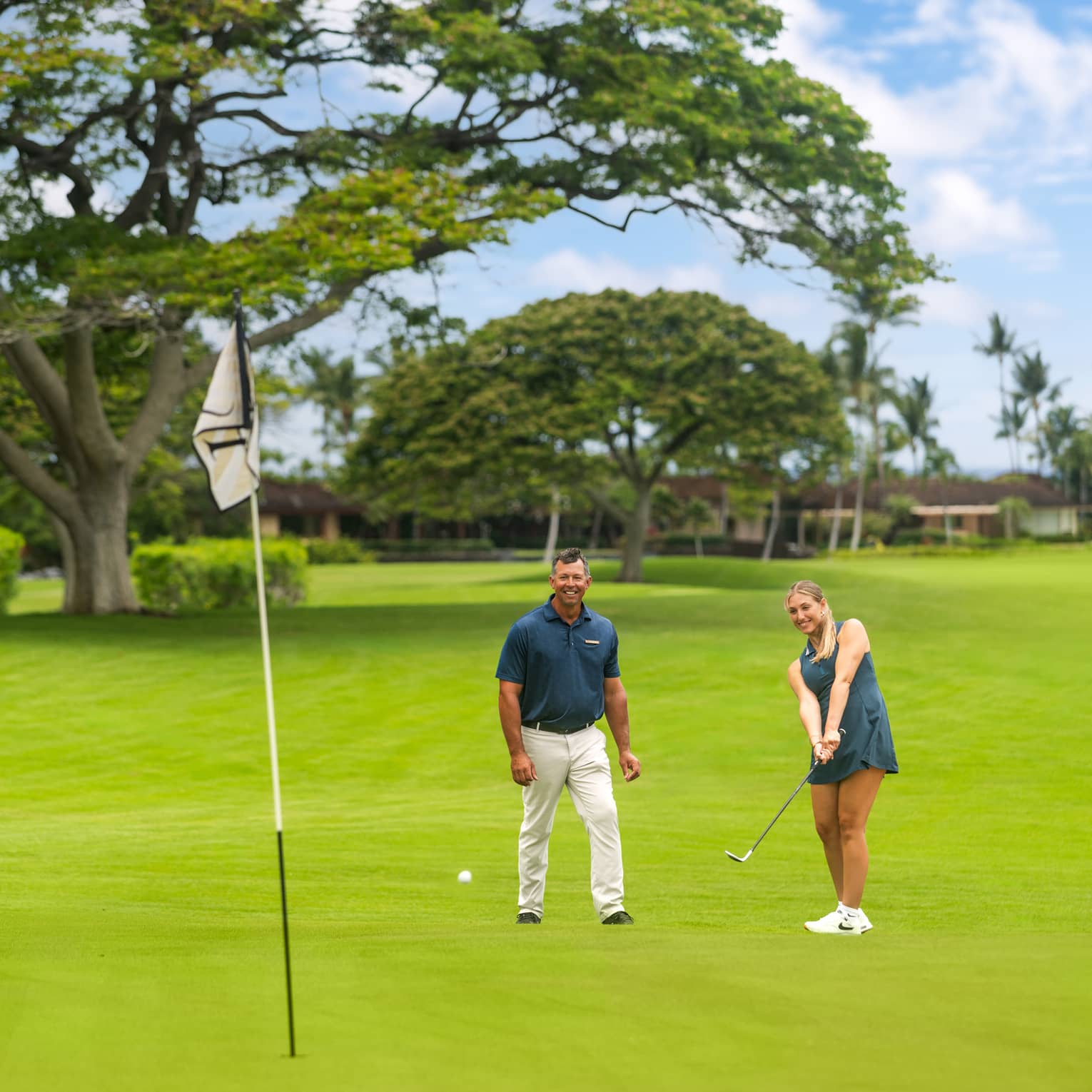 Two people on a golf course with one practicing her short game.