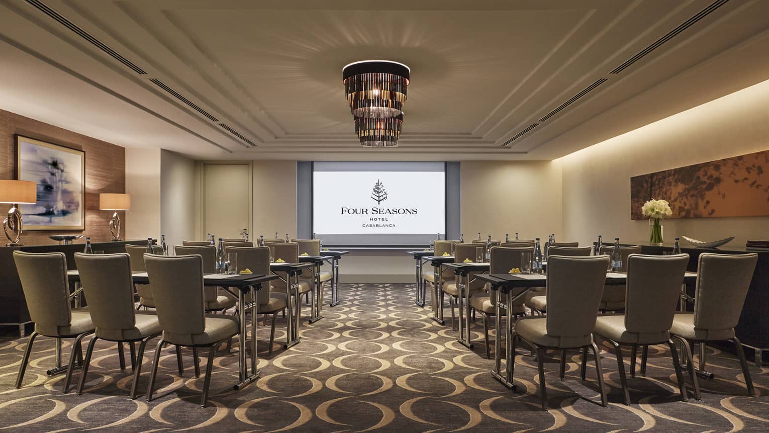 Rows of chairs, tables facing large screen with Four Seasons logo