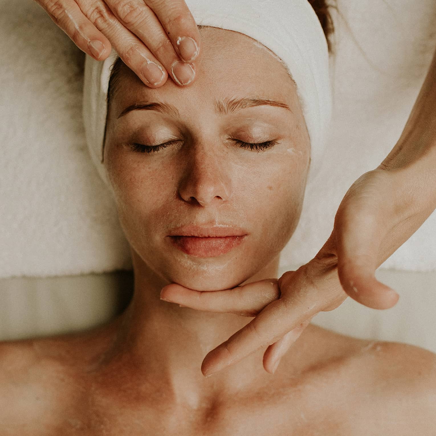 Person receiving a relaxing facial massage with eyes closed and head wrapped in a towel