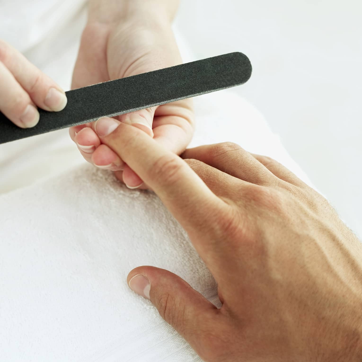 Woman holds manicure nail file to man's fingernails over white towel