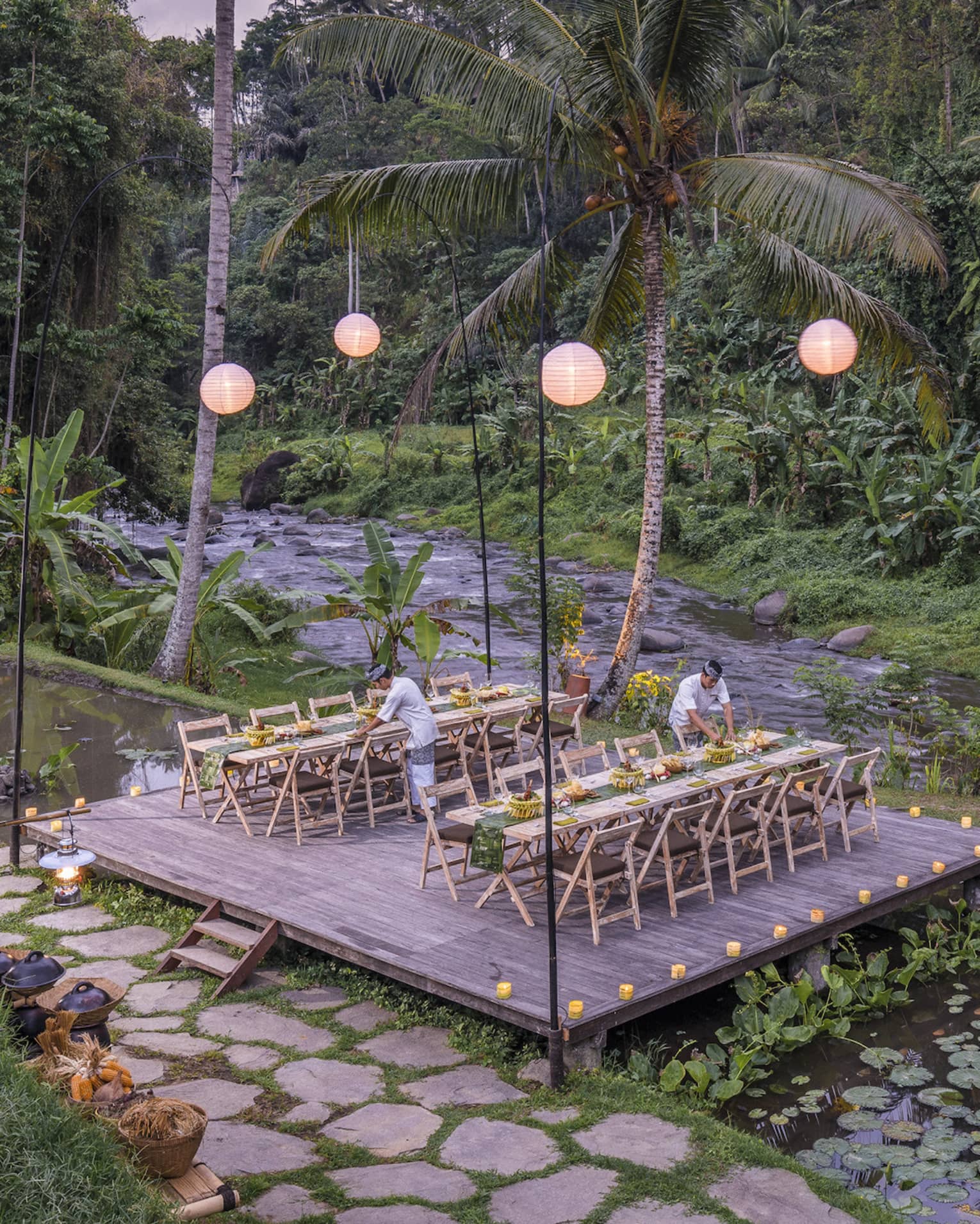Megibung Dinner is set on a wooden deck as the sun sets beyond lush trees