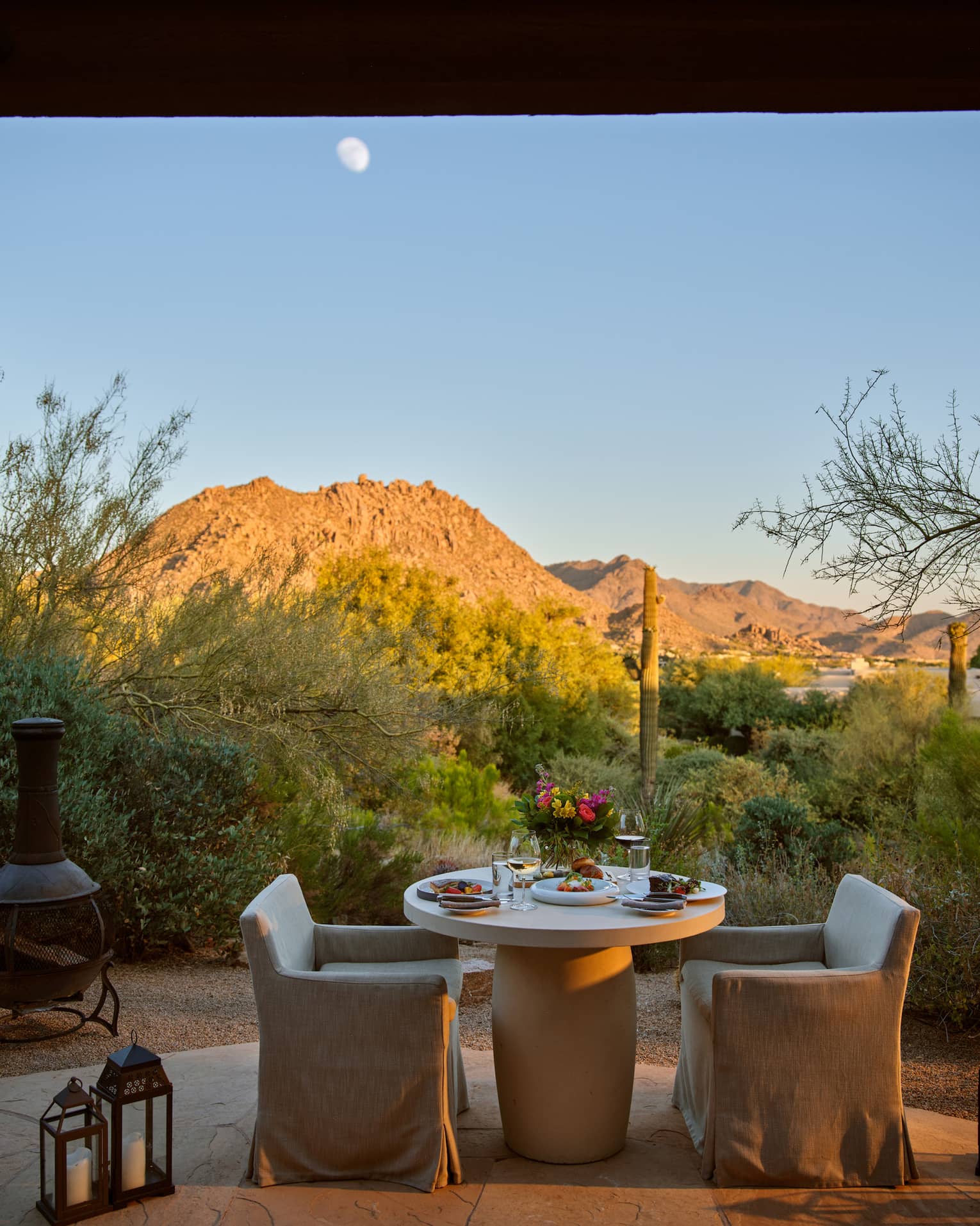 Two chairs and a table outside with lanterns and a view of the mountains.