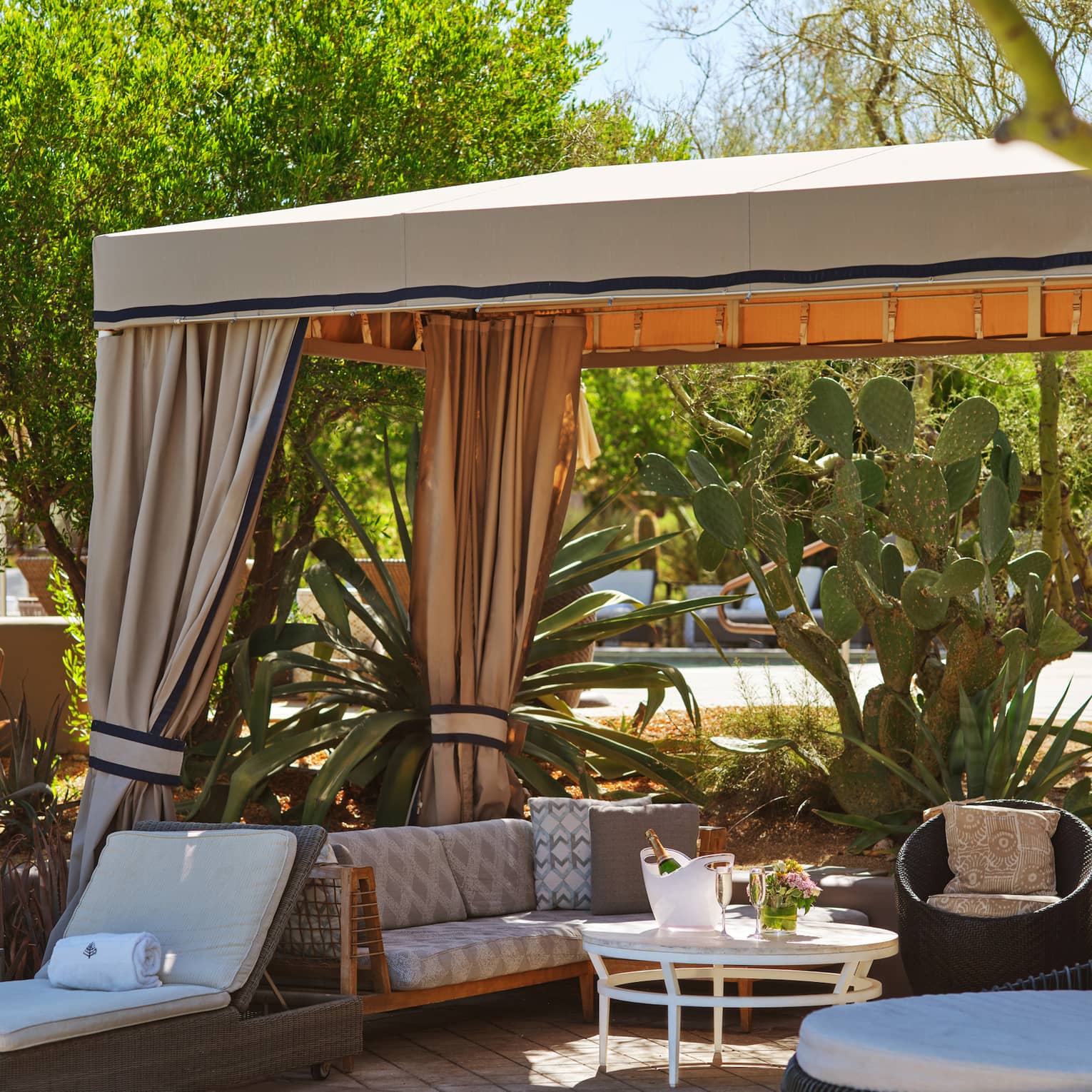 Cabana with lounge chairs, a couch, table and trees surrounding it.
