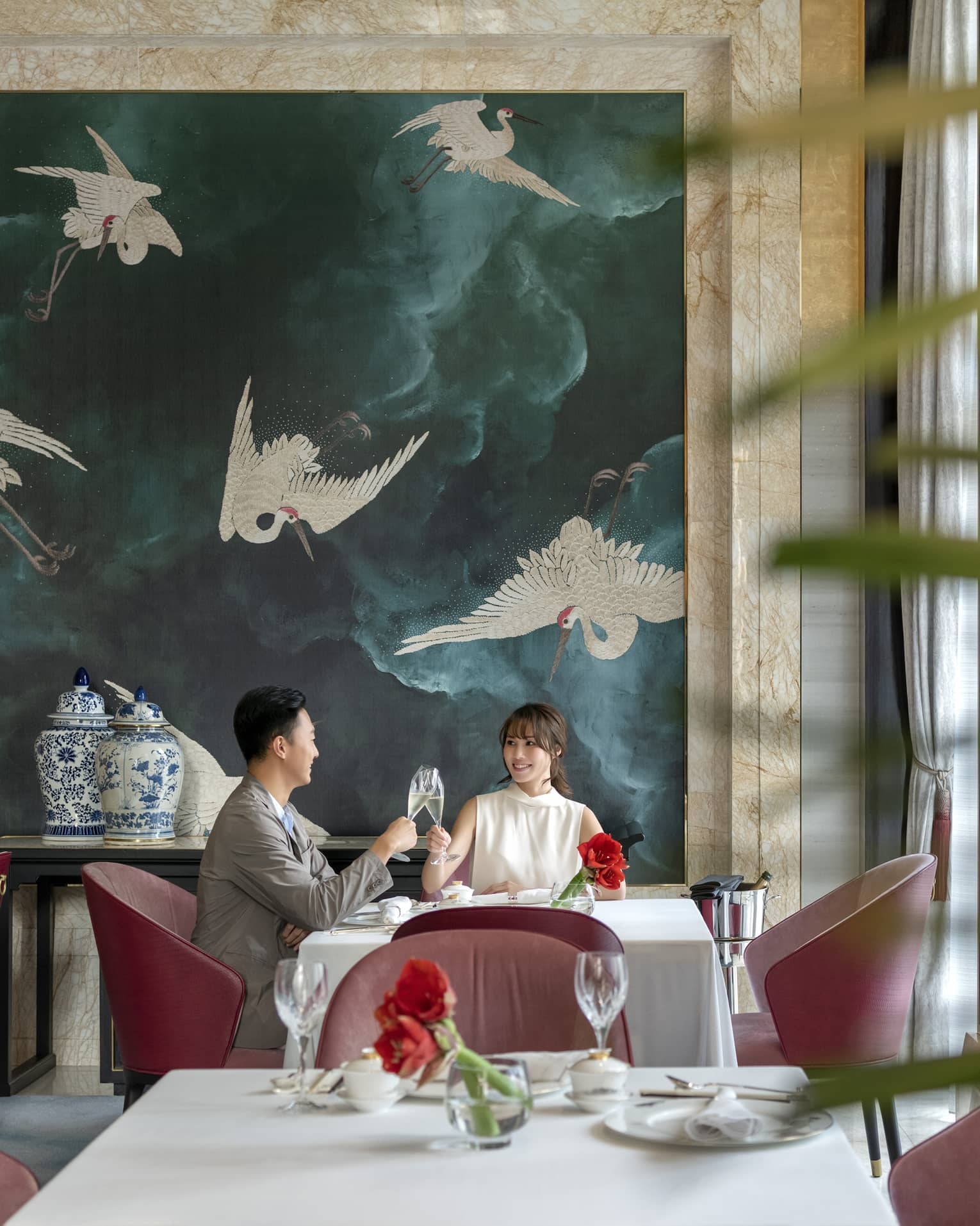 Man and woman clink glasses at table in Zi Yat Heen restaurant at Four Seasons Hotel Macao Cotai Strip