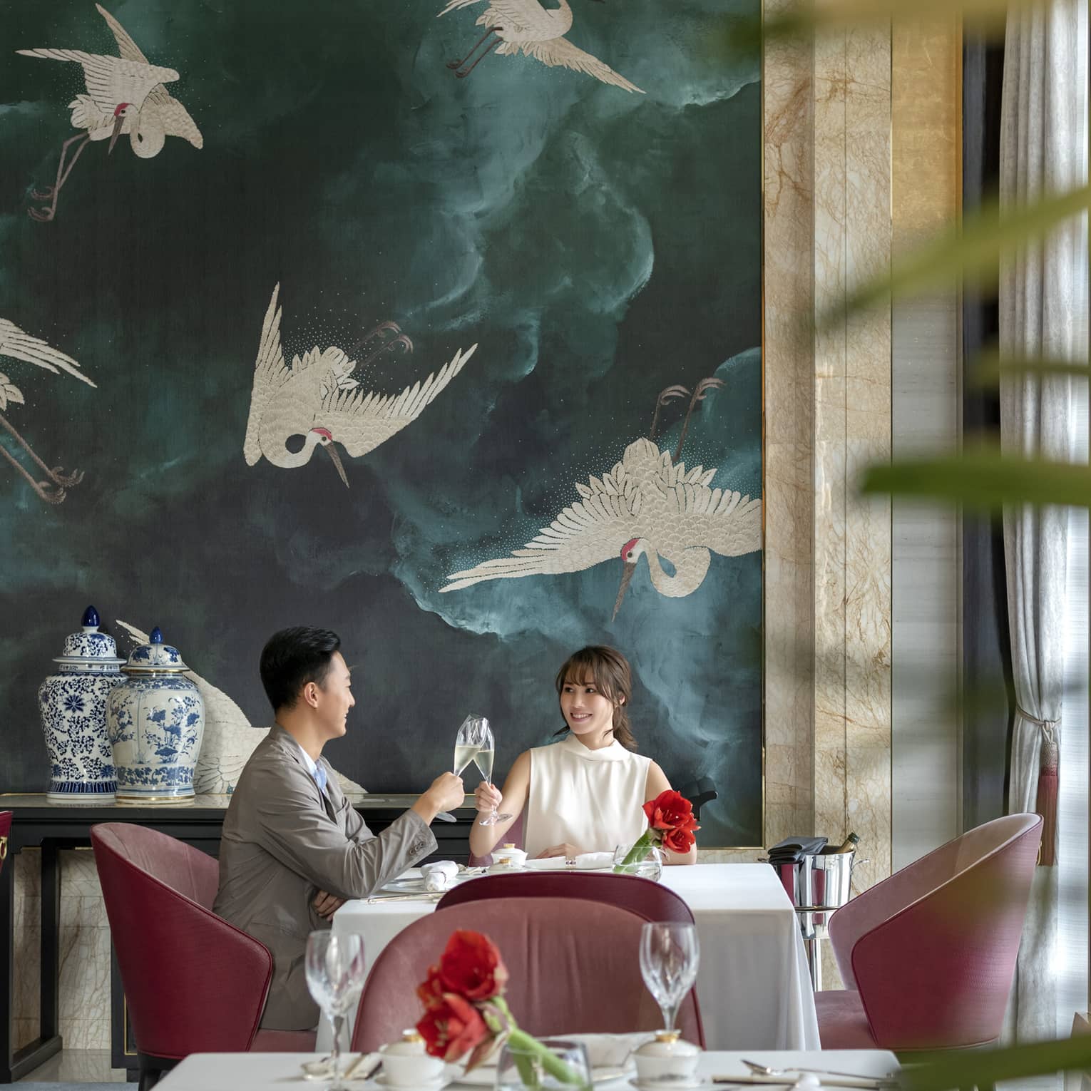 Man and woman clink glasses at table in Zi Yat Heen restaurant at Four Seasons Hotel Macao Cotai Strip