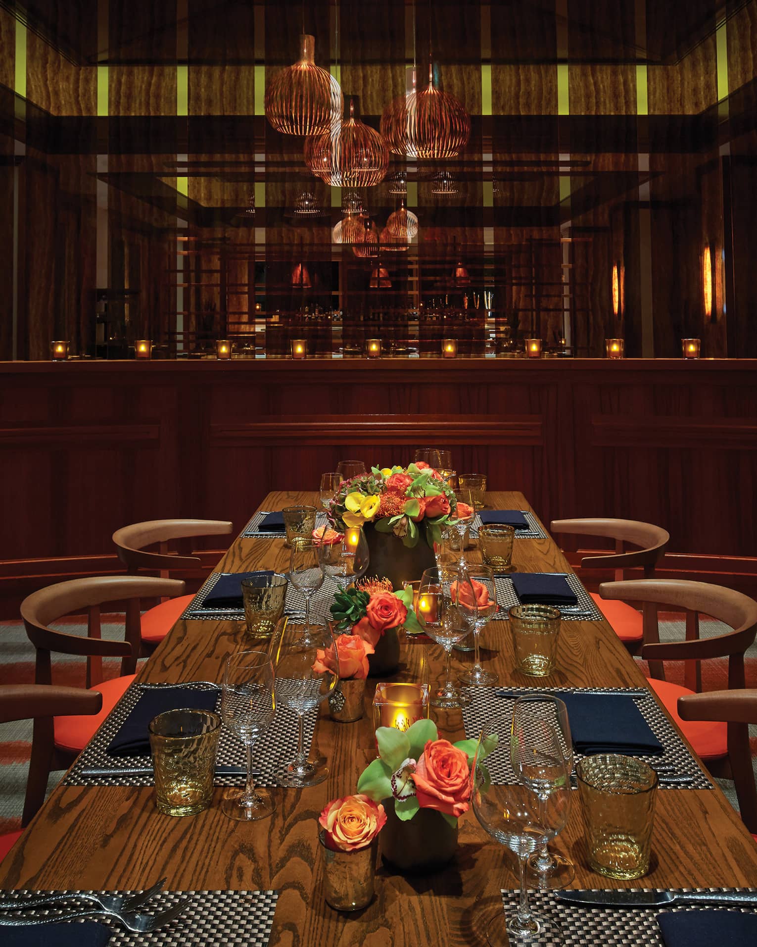 Basket lights hang above a long private dining table with candles, flowers and place-settings 