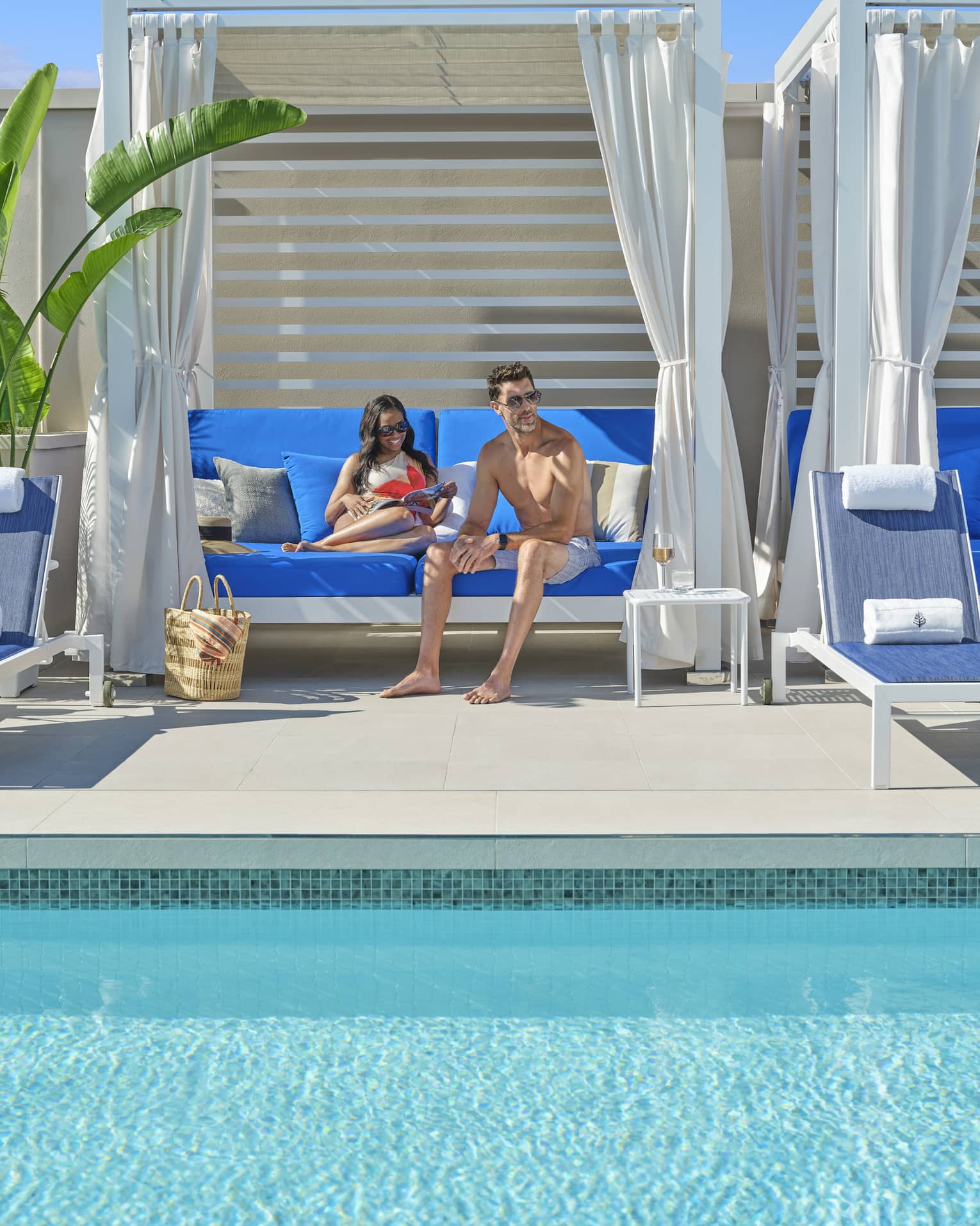 Two guests sitting on a blue couch in a cabana by the pool.