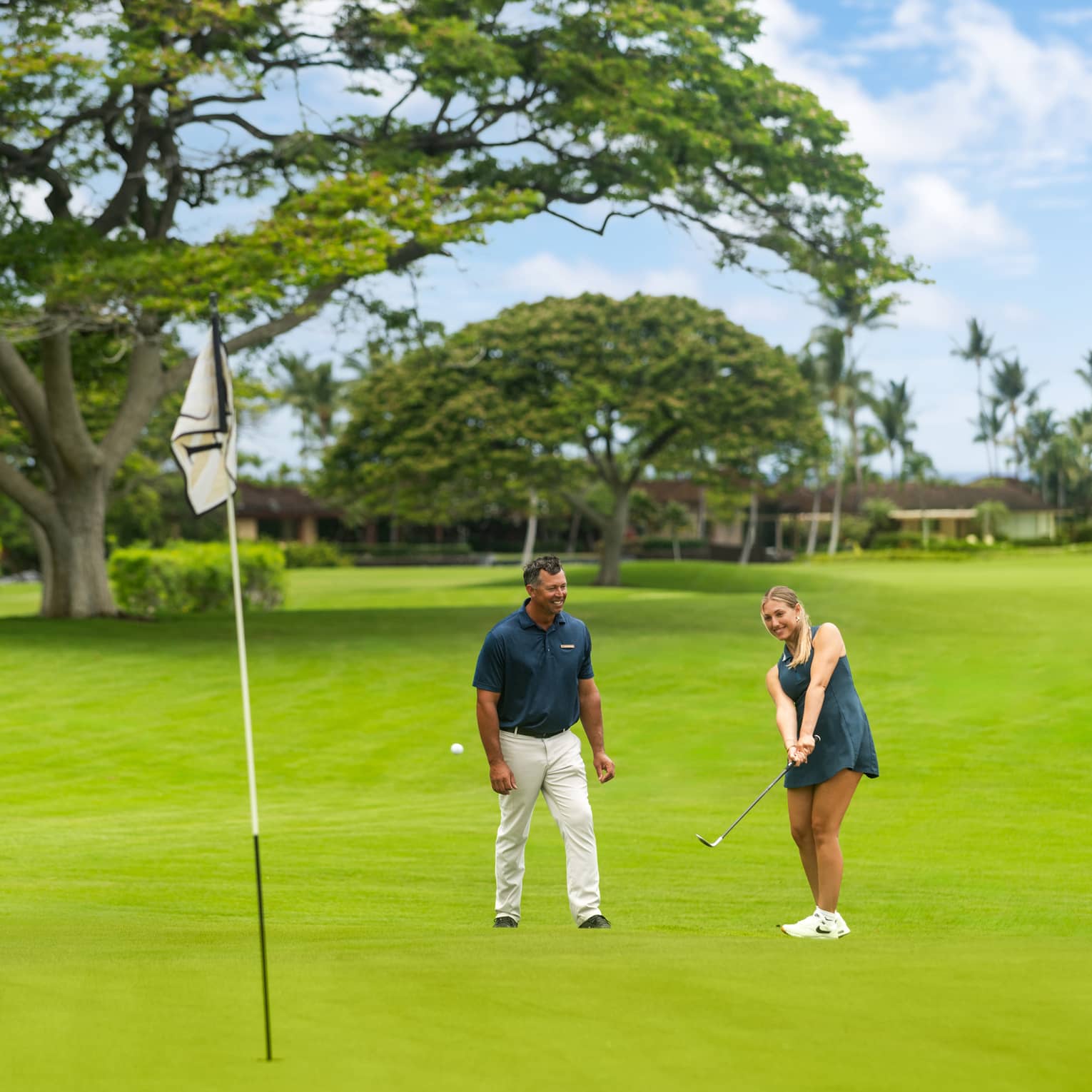 Two people on a golf course with one practicing her short game.