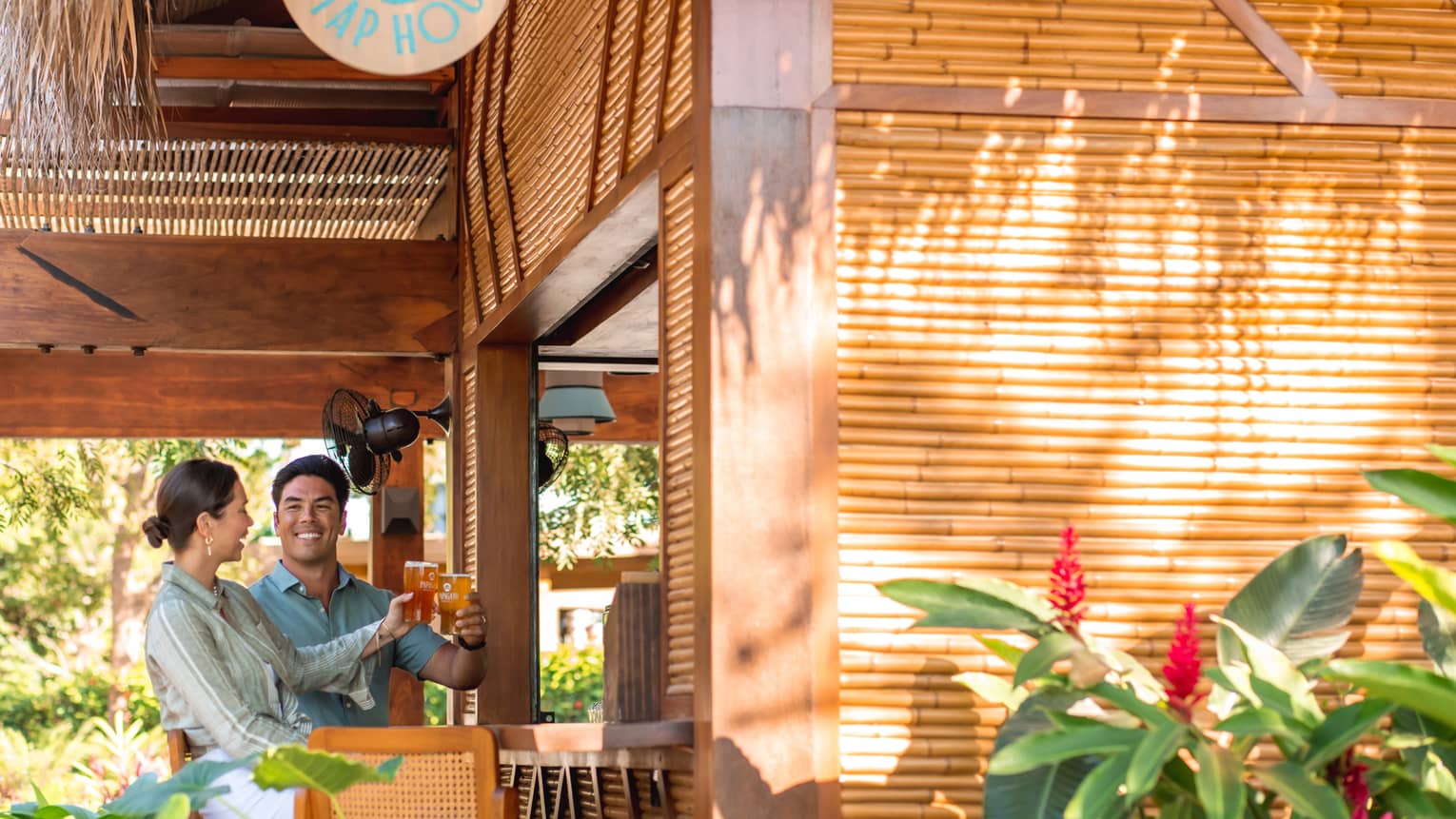 Two people raising a pint of beer to each other at the all-bamboo bar at Palapita Taphouse