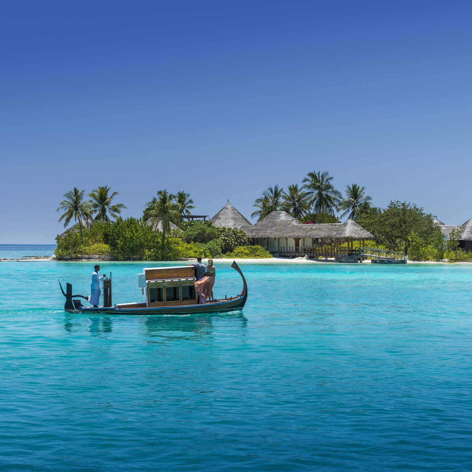 A wooden boat with passengers travels over clear turquoise water toward a tropical island spa with palm trees and thatched-roof villas