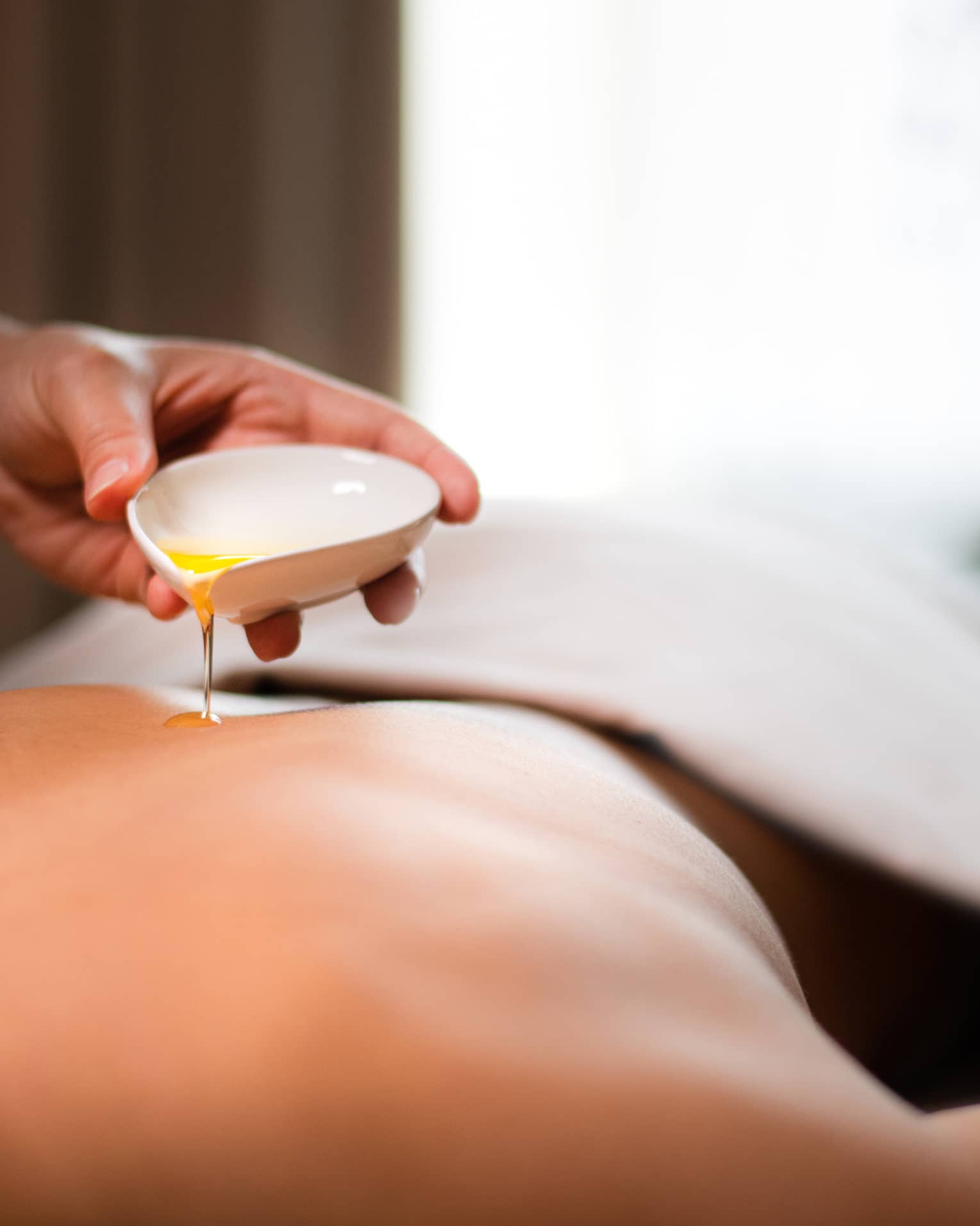 A spa staff member pouring liquid onto a woman?s back.