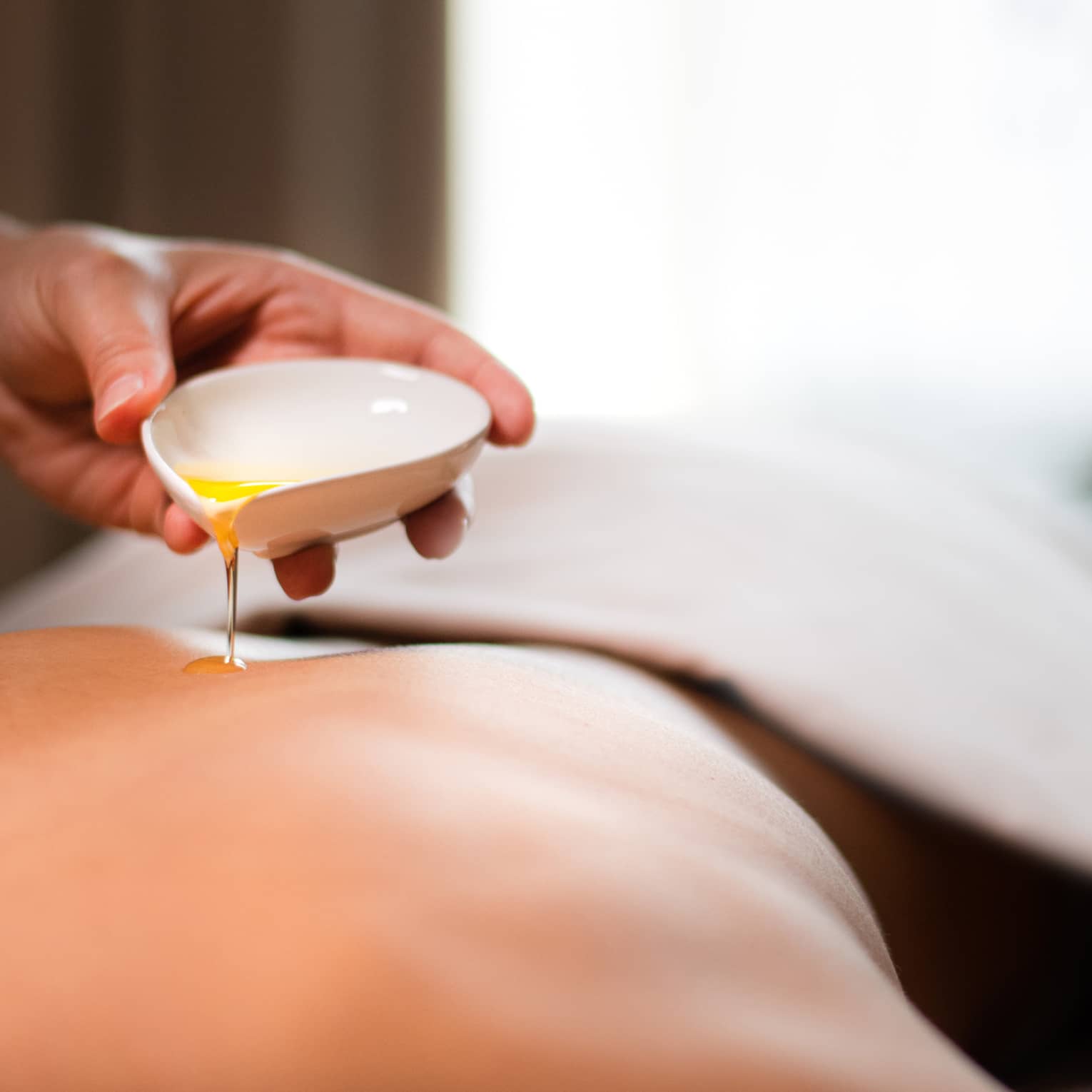 A spa staff member pouring liquid onto a woman?s back.