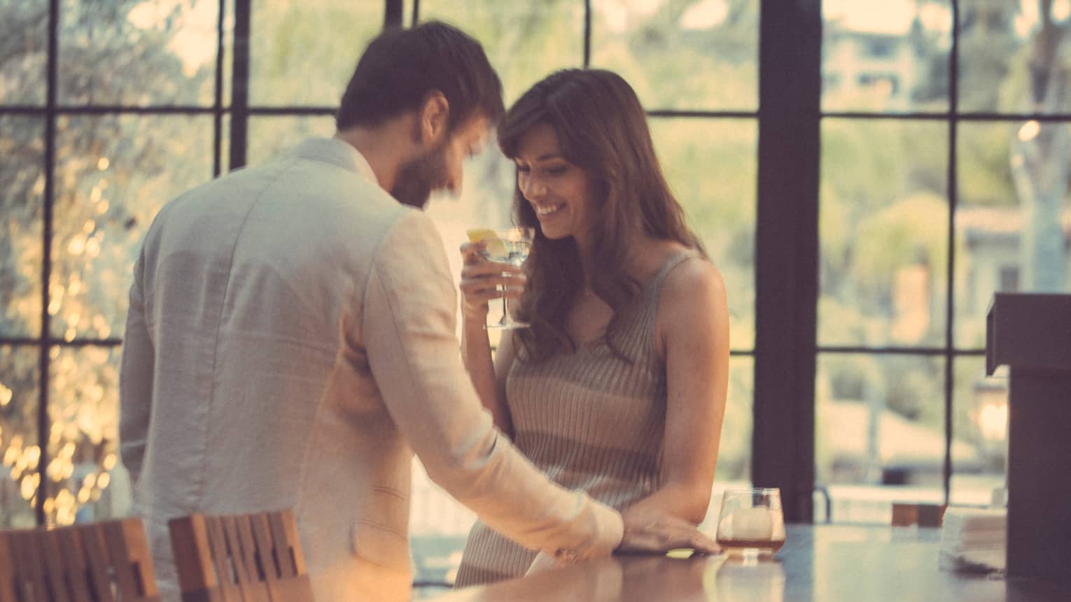 Couple stands at the bar smiling, woman with martini in hand