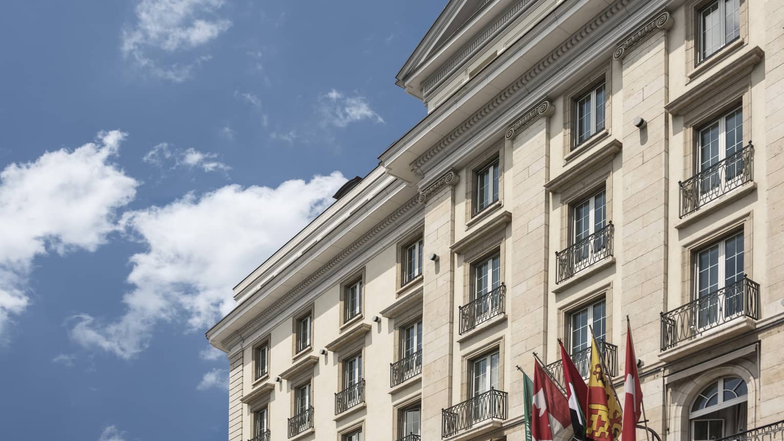 Top of Four Seasons Hotel Geneva exterior with group of flags against blue sky