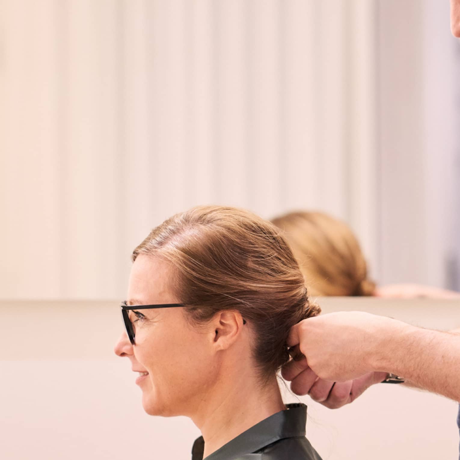 Woman sits in salon chair as hair stylist with long beard holds her hair