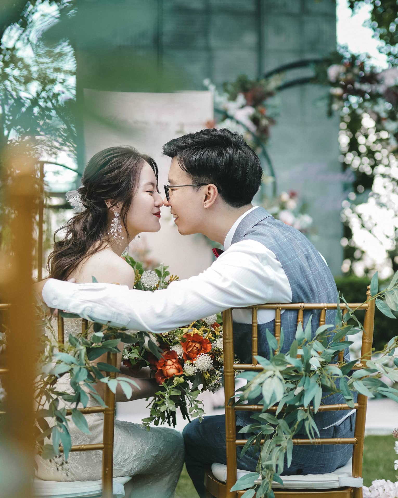 Bride and groom lean in for a kiss at garden wedding dining table surrounded by flowers
