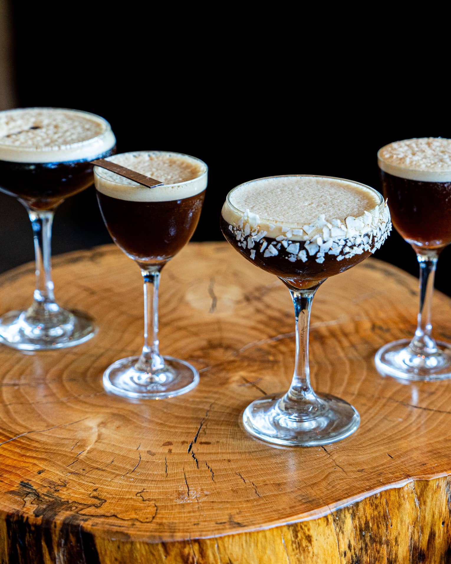 Four espresso martinis on a small wood table.