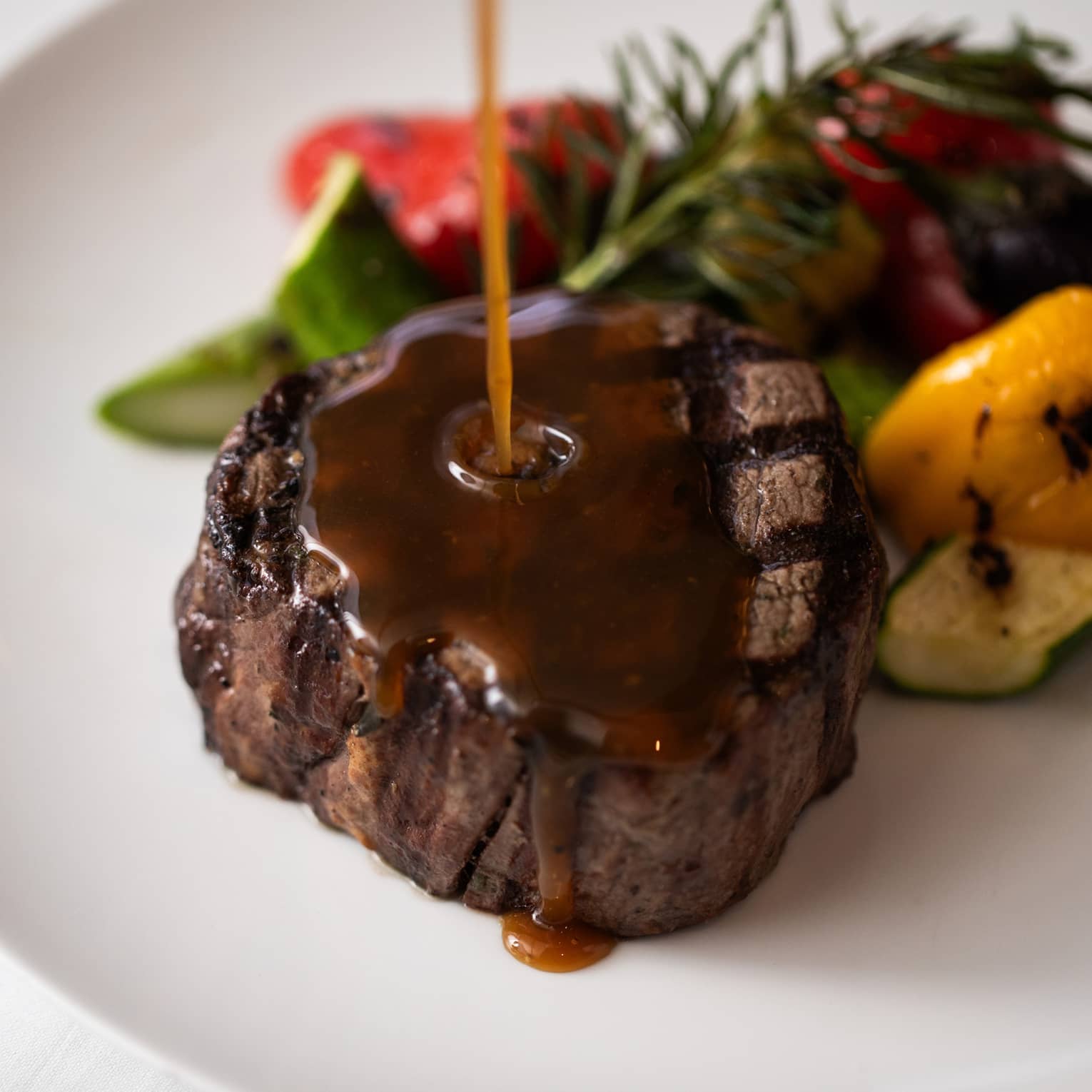 Grilled beef being drizzled with sauce next to a serving of vegetables