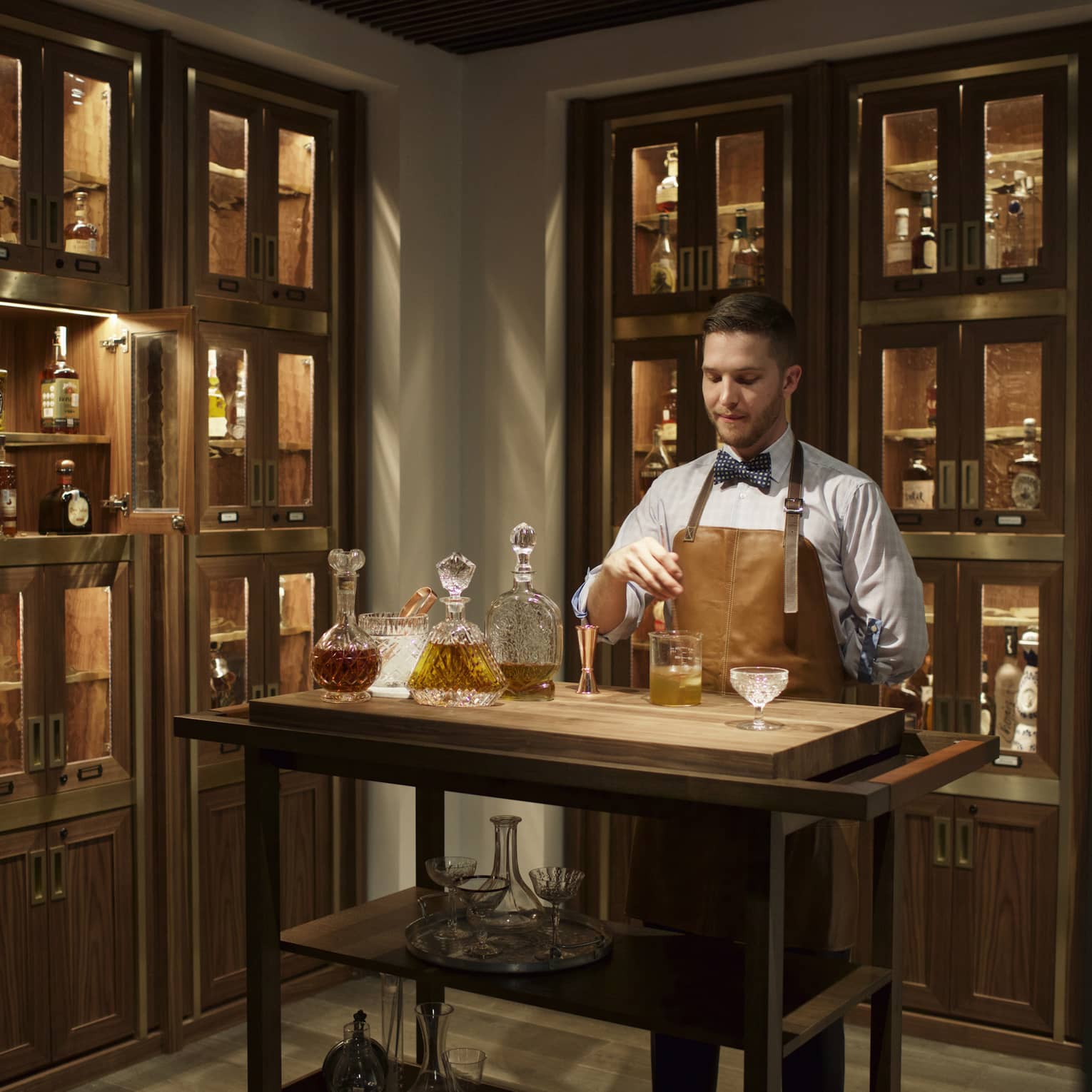 Bayou & Bottle mixologist in apron stirs bourbon cocktail, surrounded by illuminated display cases with bottles