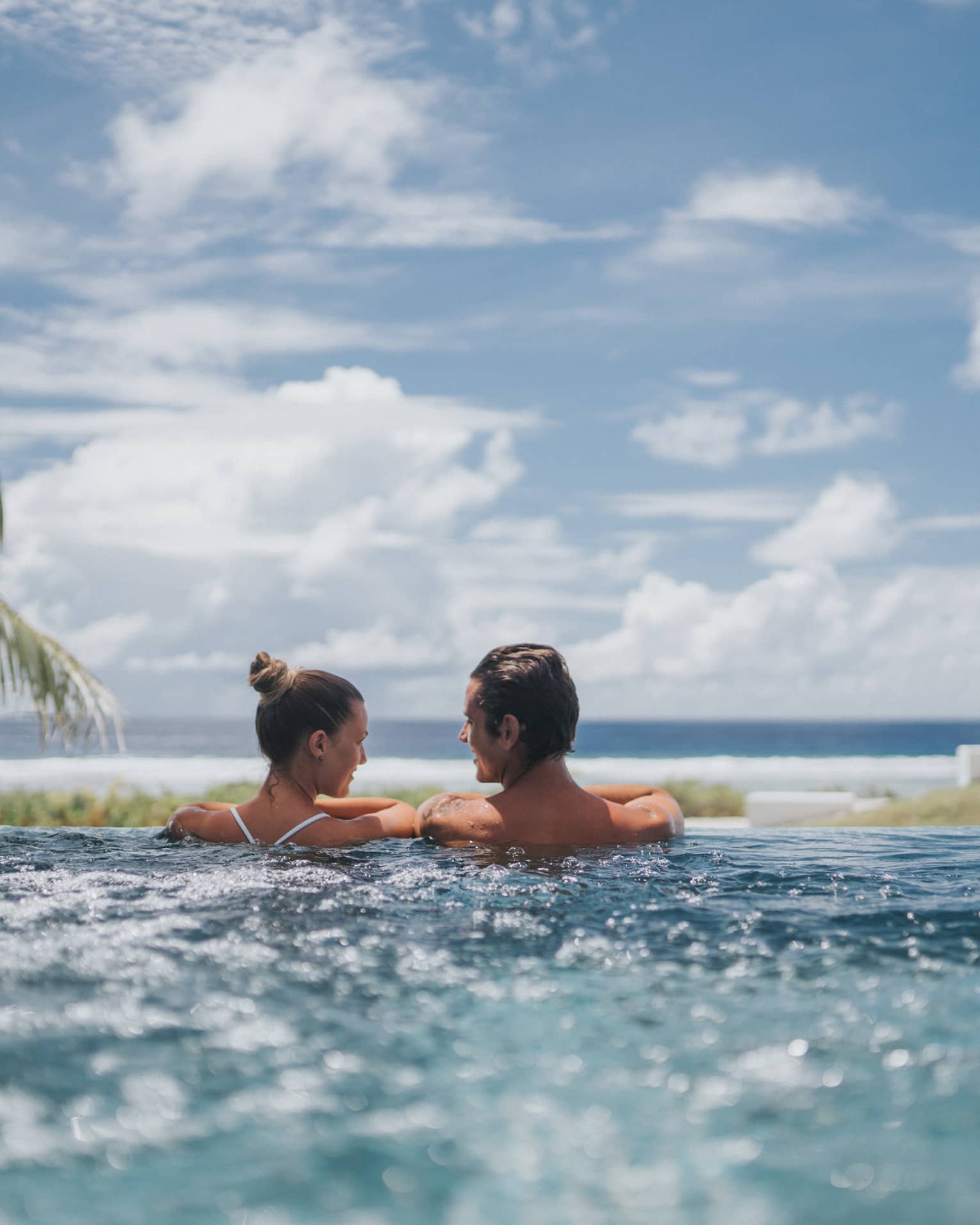 Back of couple at edge of whirlpool overlooking ocean, blue sky