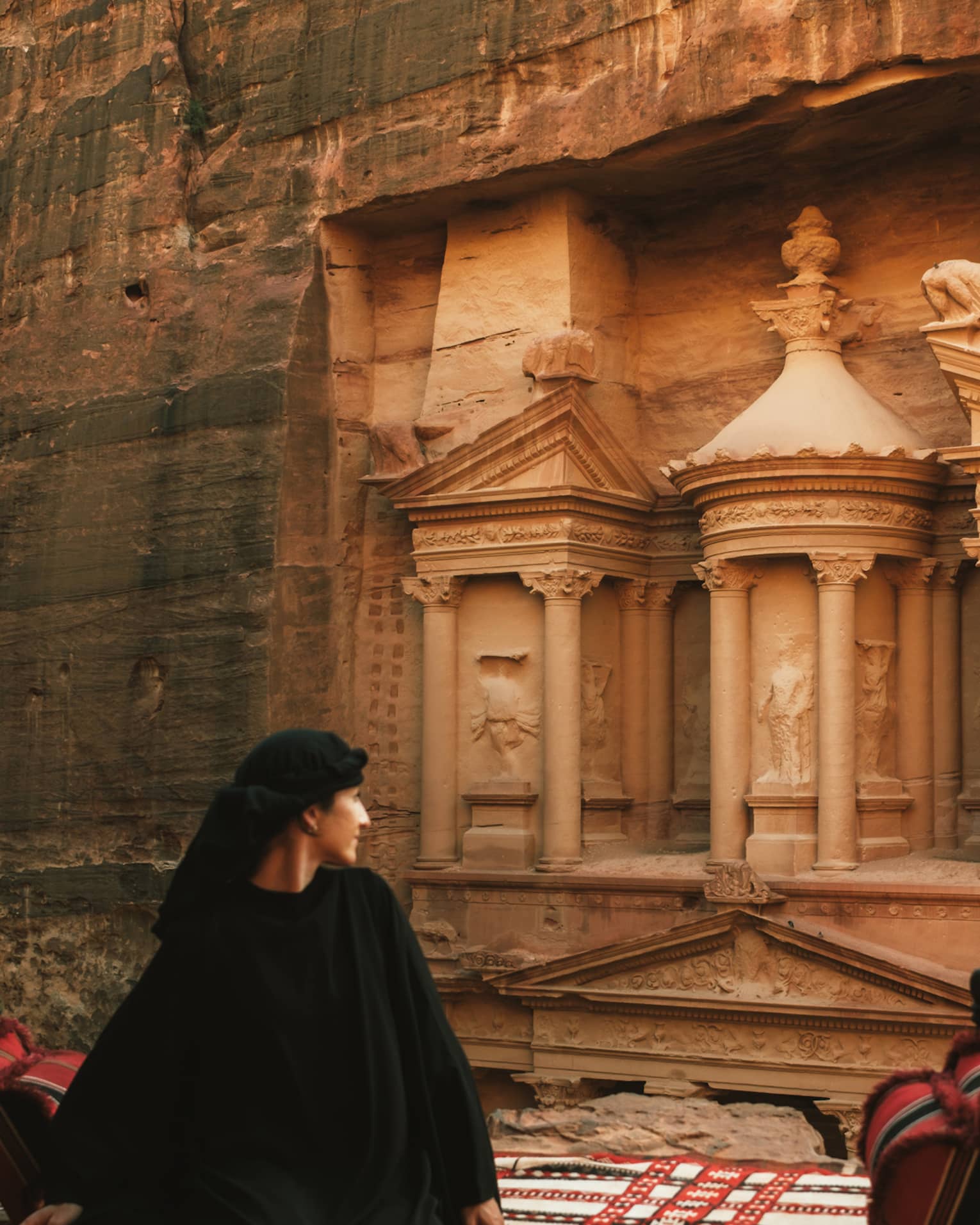 A person stands looking at buildings carved into a red rock cliffside.