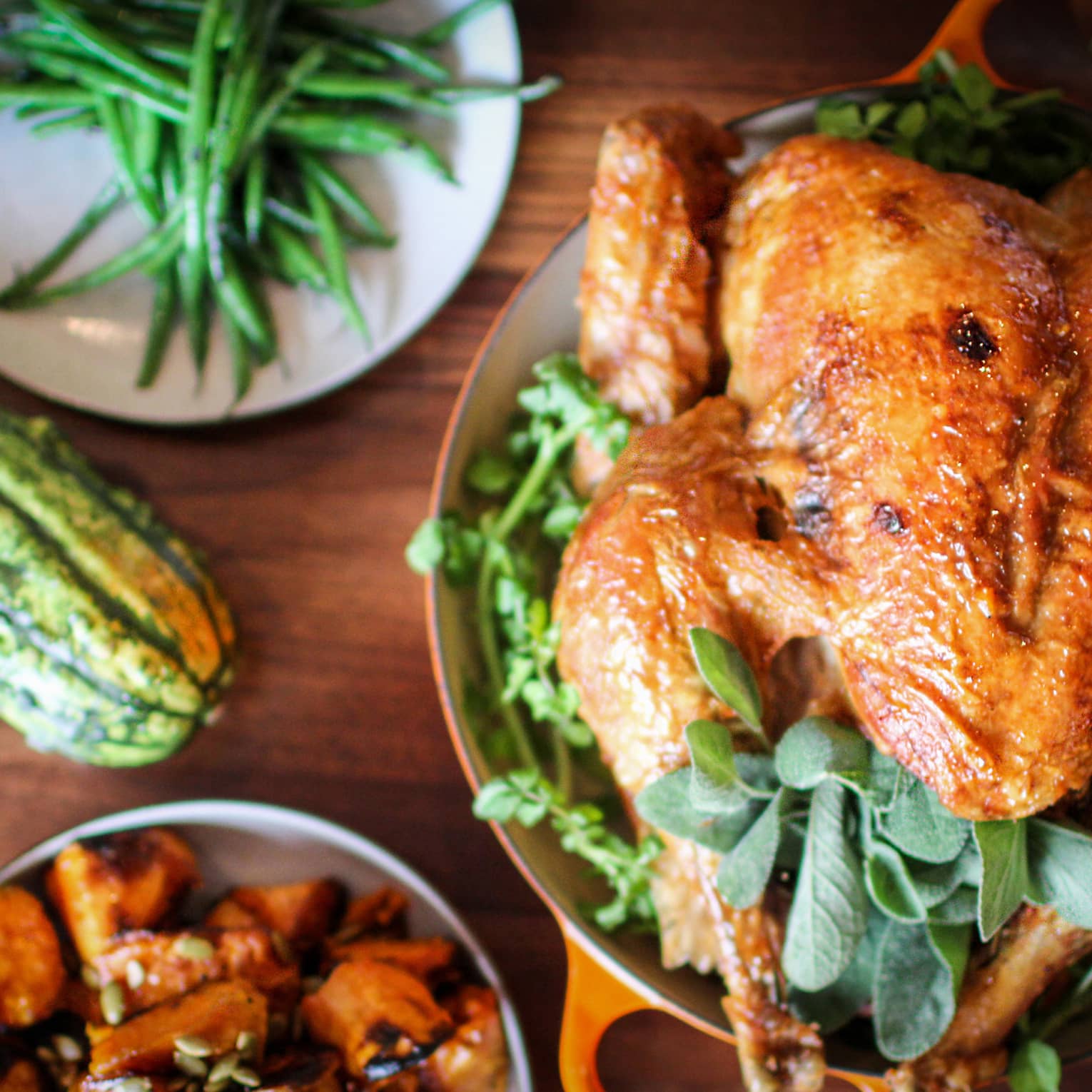 Roast turkey with fresh herbs on platter, presented on wood tabletop with gourds and green beans on white plate