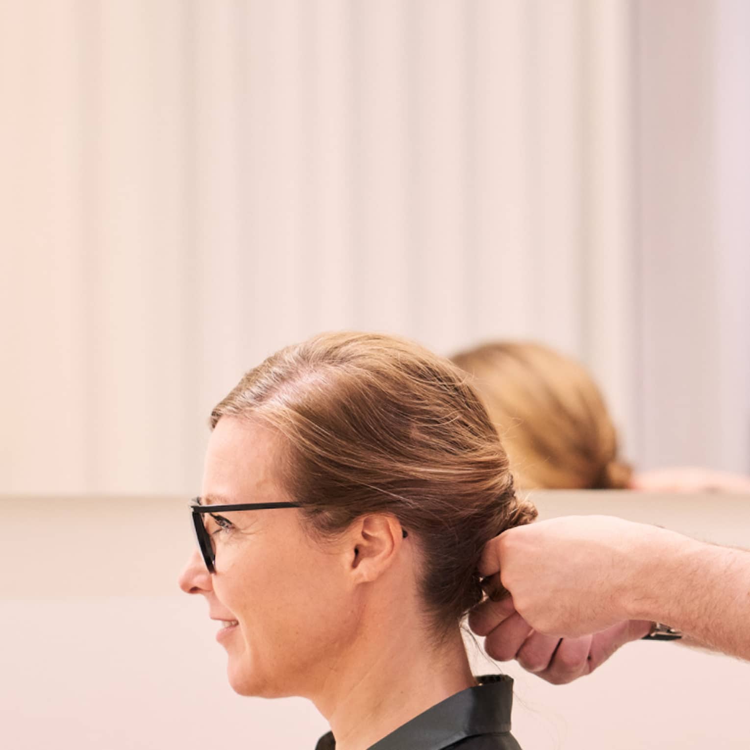 Woman sits in salon chair as hair stylist with long beard holds her hair