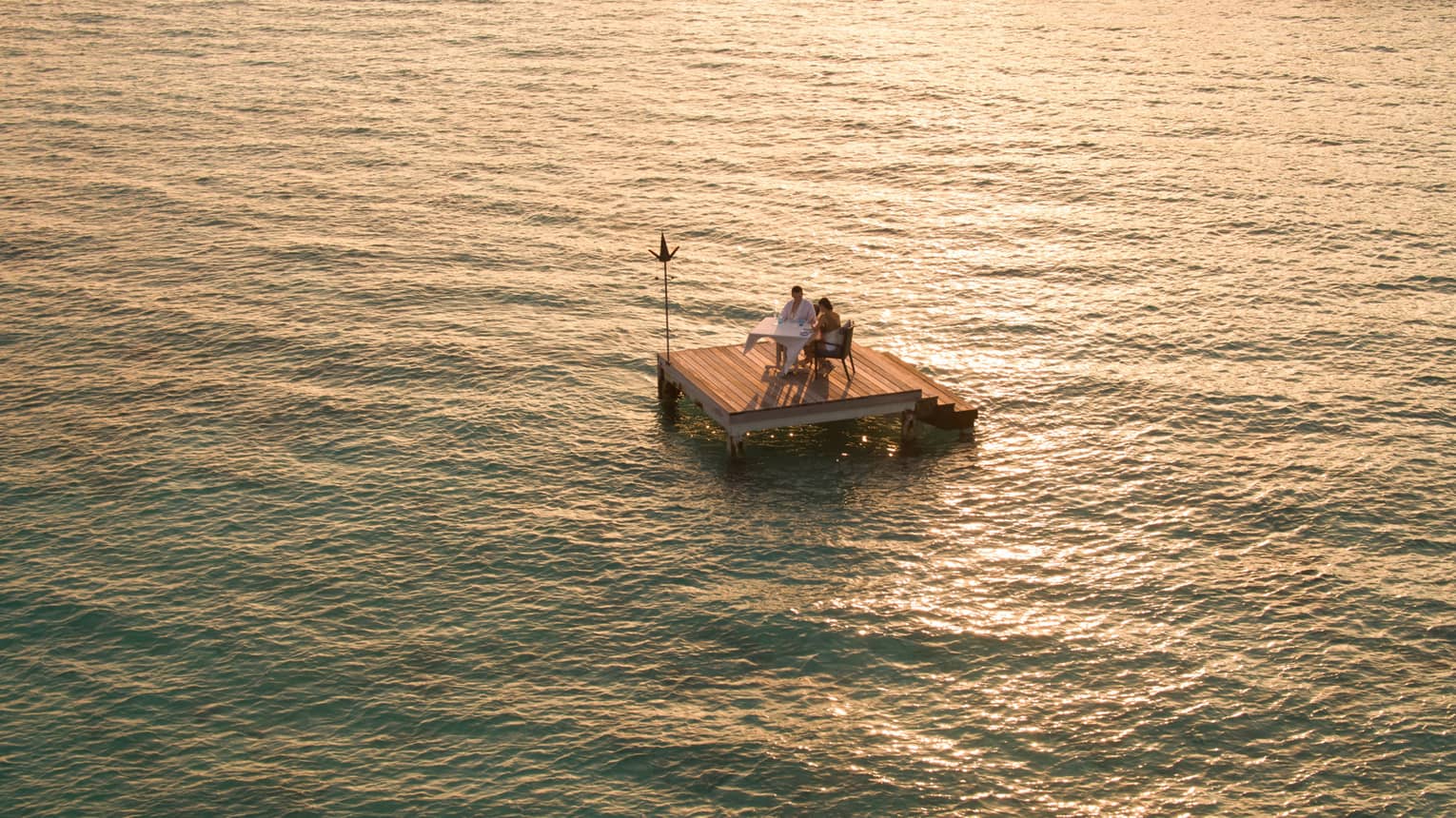 Aerial view of couple dining on small floating wood platform on moonlit lagoon