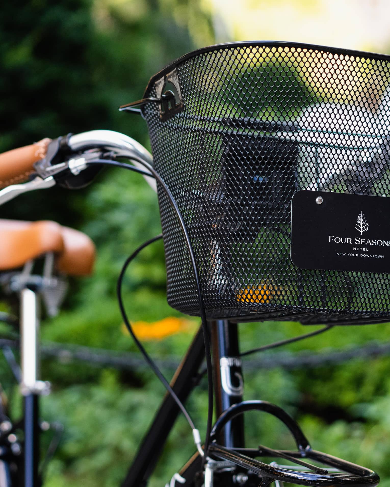 A bike with a black basket at the front that says "Four Seasons" outside by plants.