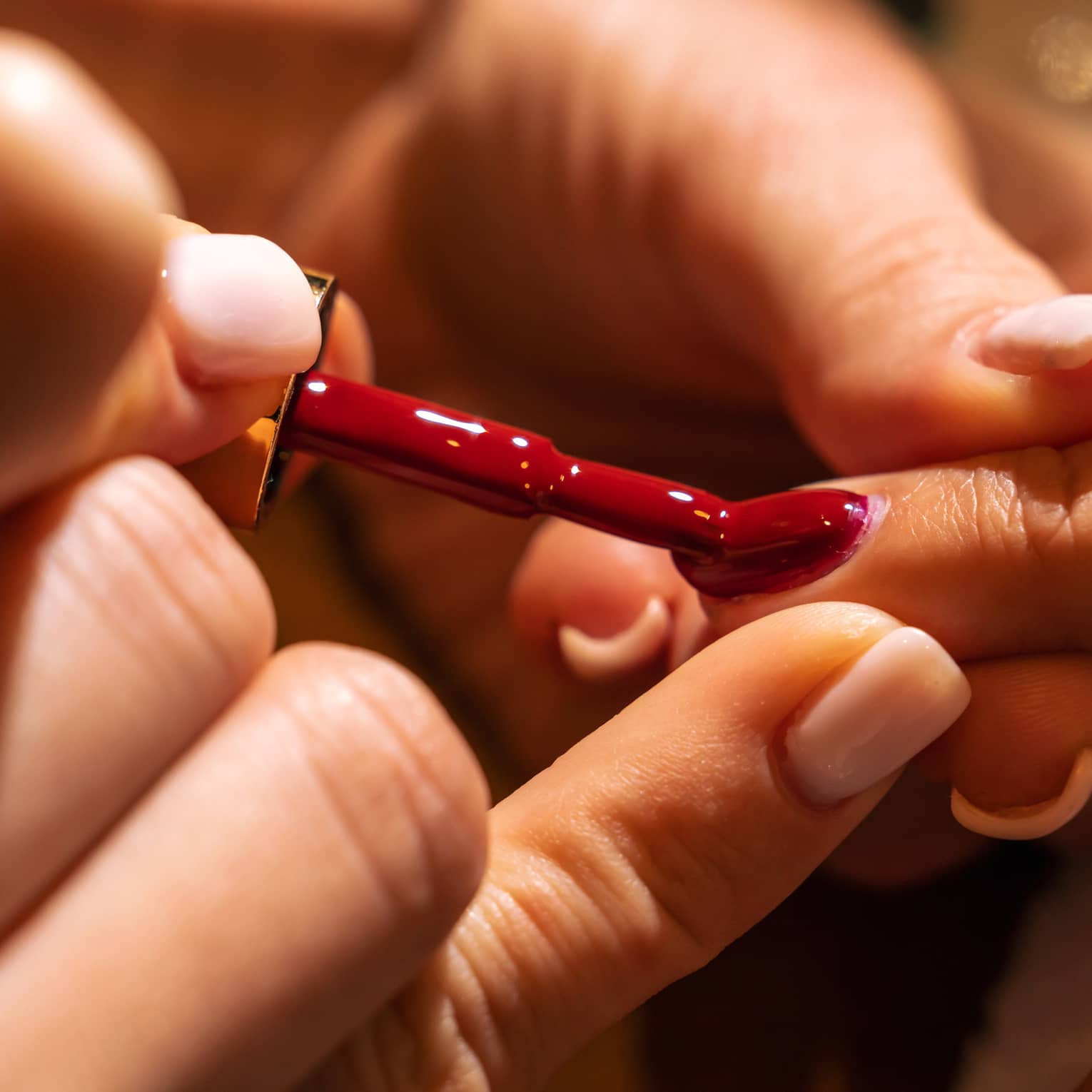 Manicurist holds a person's finger as they apply bright red nail polish to a nail