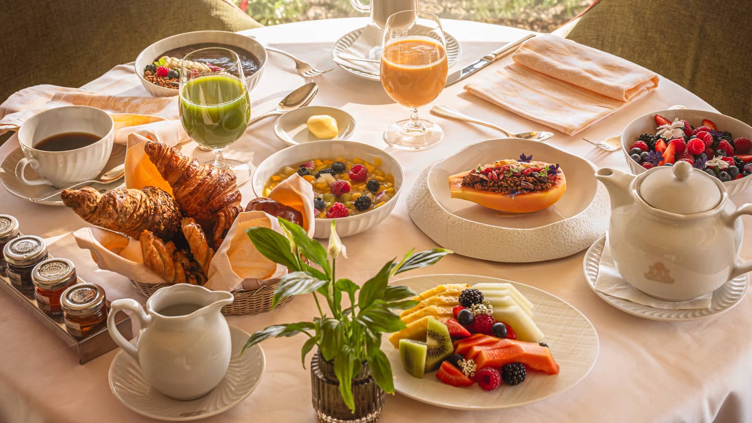 A round table in front of a window, set with an array of brunch dishes and beverages