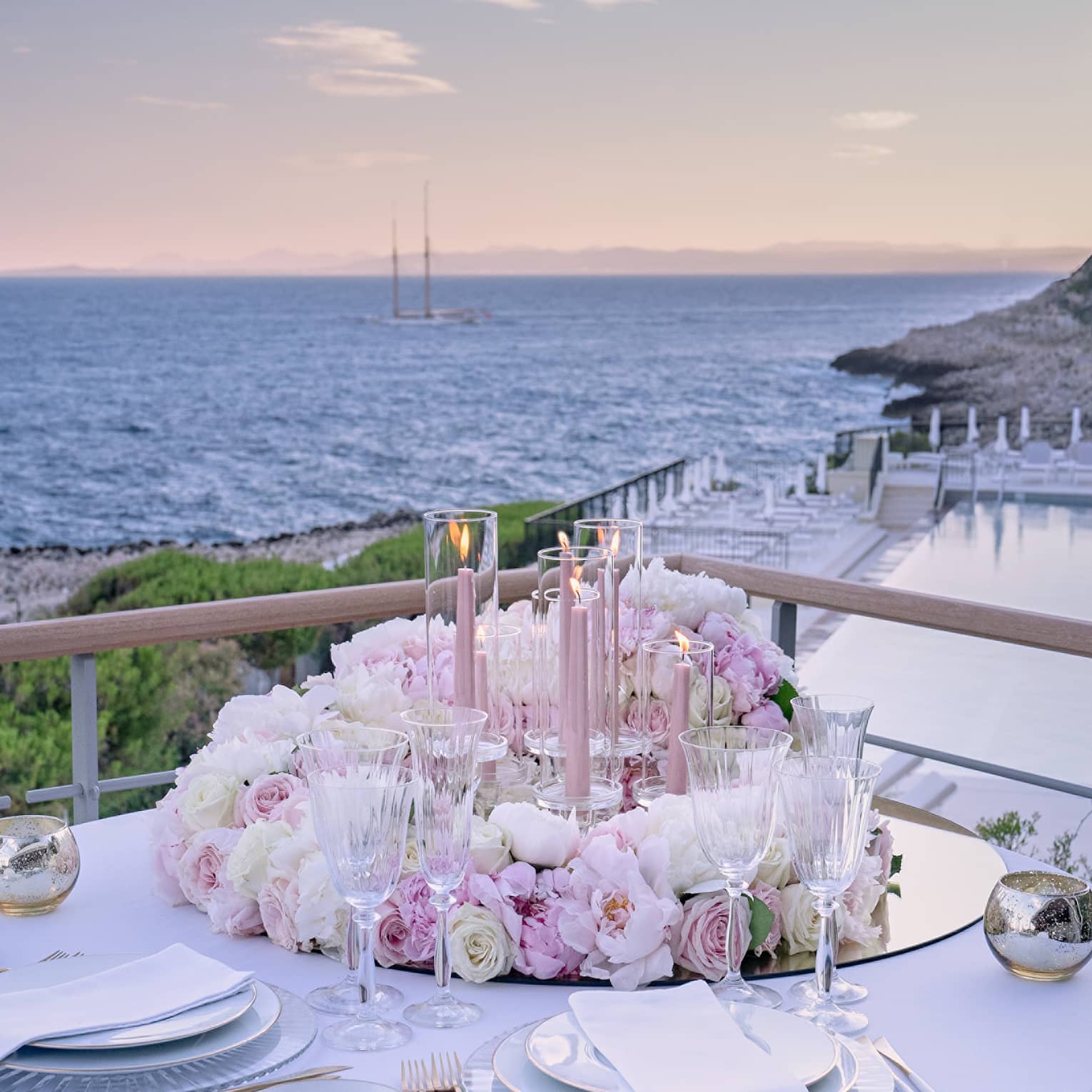 Balcony with round set table, pink floral arrangement, water views at sunset
