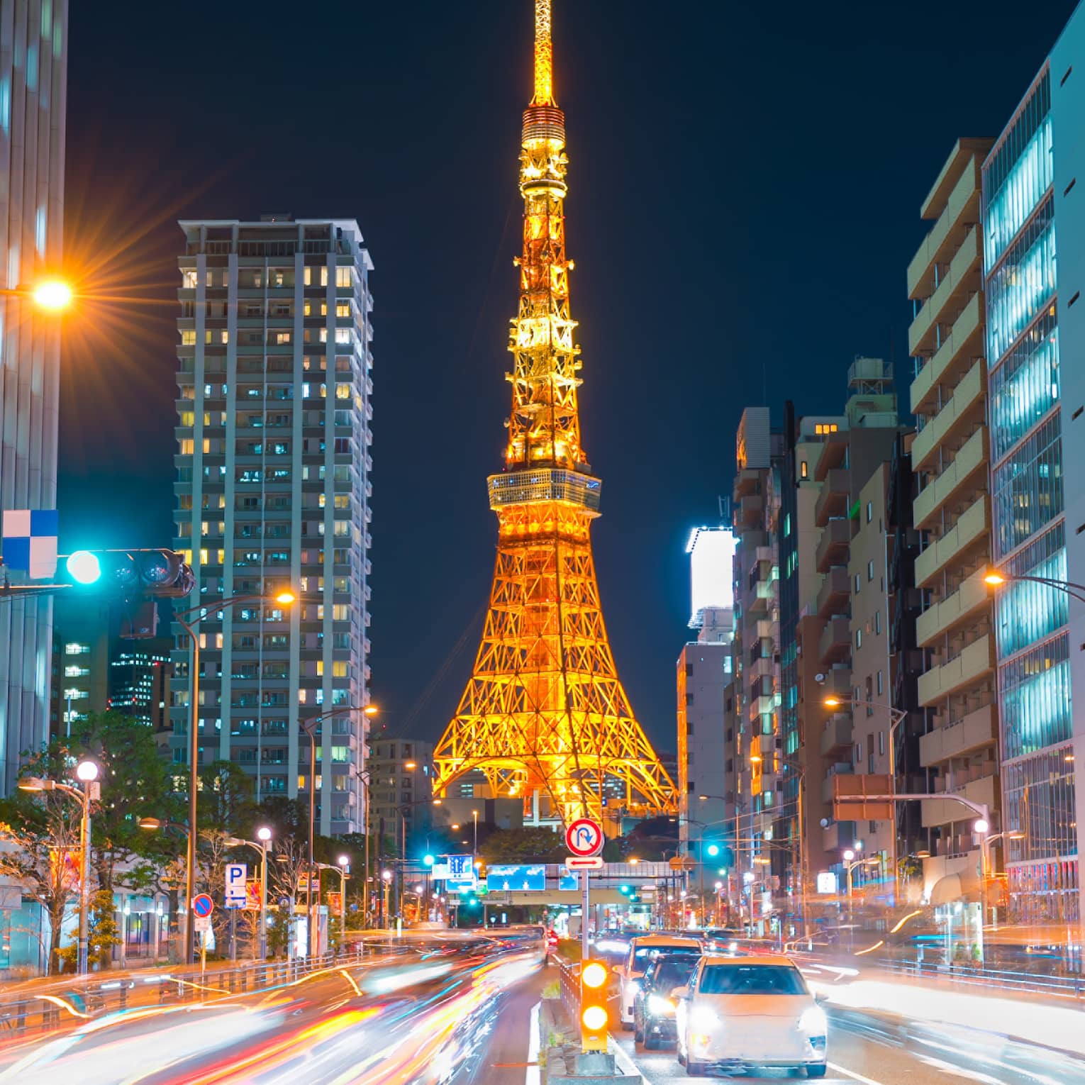 Long view down a brightly-lit street, the Tokyo Tower at the bottom, glowing in orangey hues against an inky-black sky.