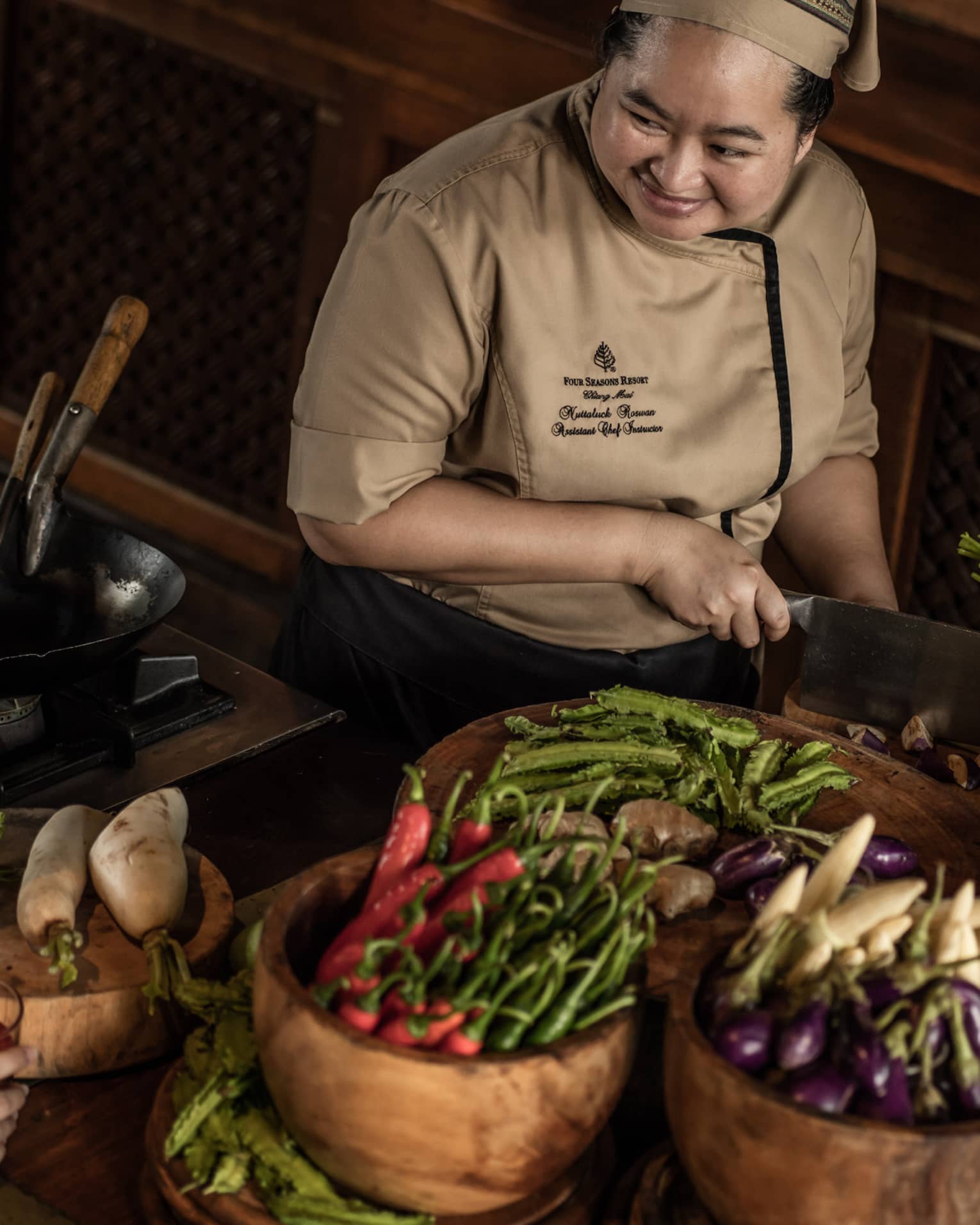 A chef teaching two participants in a cooking class, surrounded by fresh vegetables and ingredients in a rustic kitchen setting.