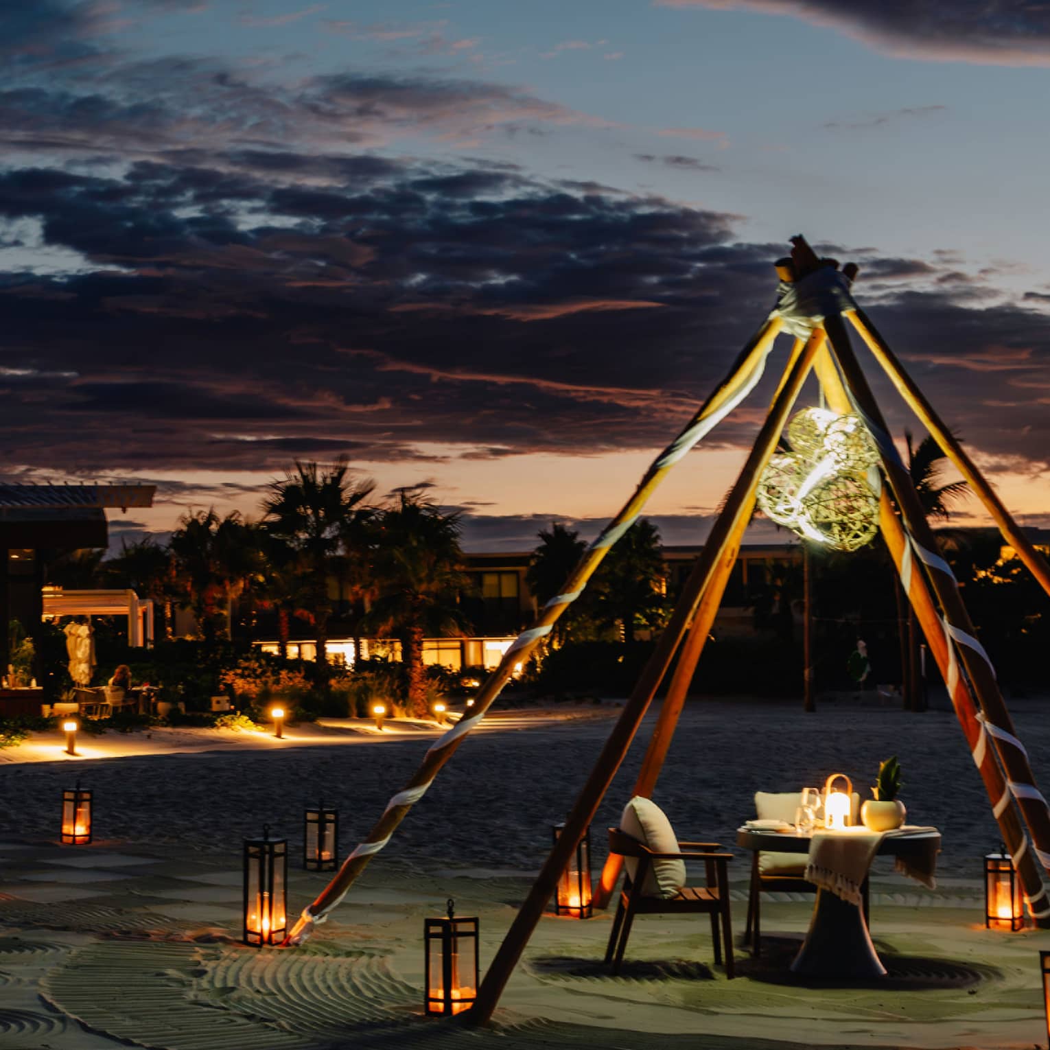 Outdoor tent with a chair and dining table, surrounded by lanterns on the ground in the evening.
