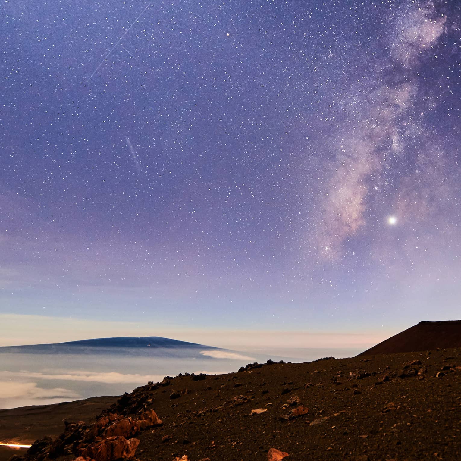 Sunrise under starry sky above mountain, volcanic rocks