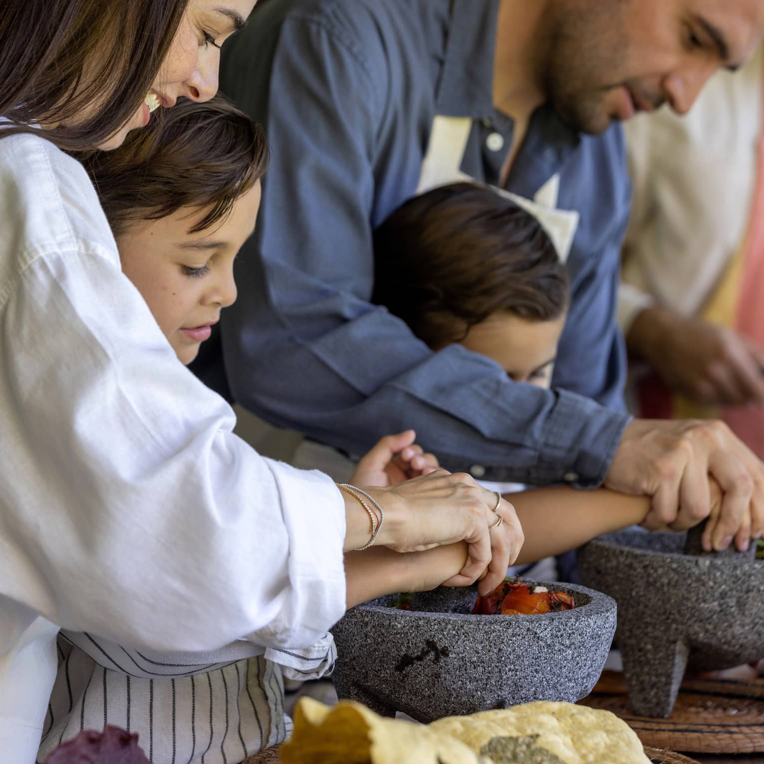 Two adult guests helping two young guests cook.