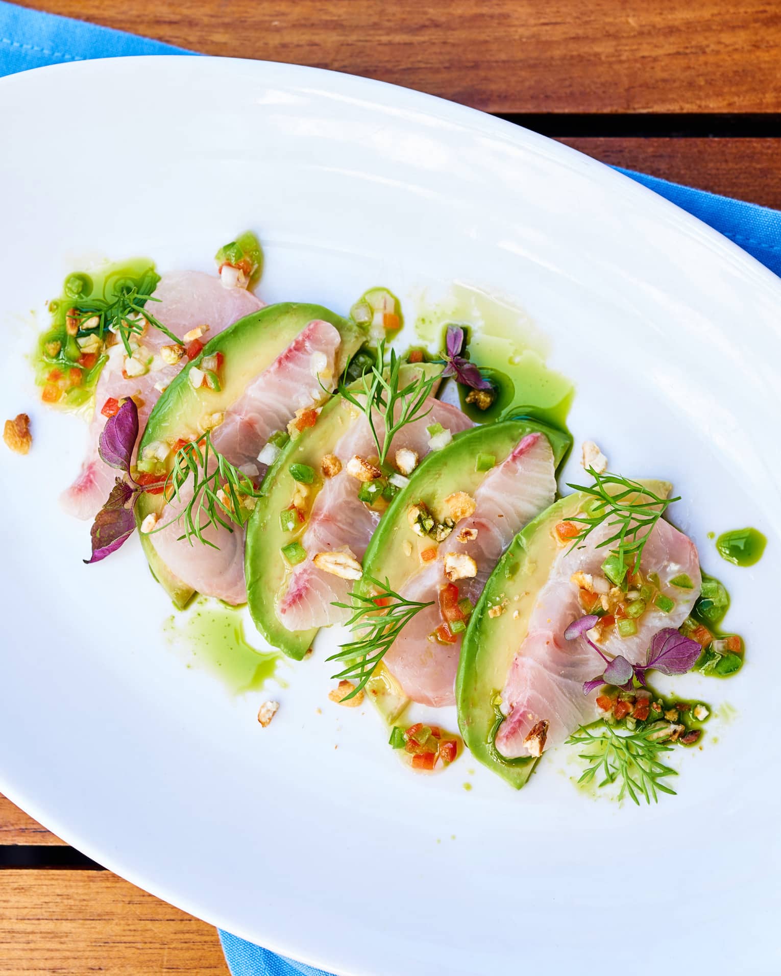 Kanpachi Crudo sliced fish arranged with avocado, toasted corn, greens
