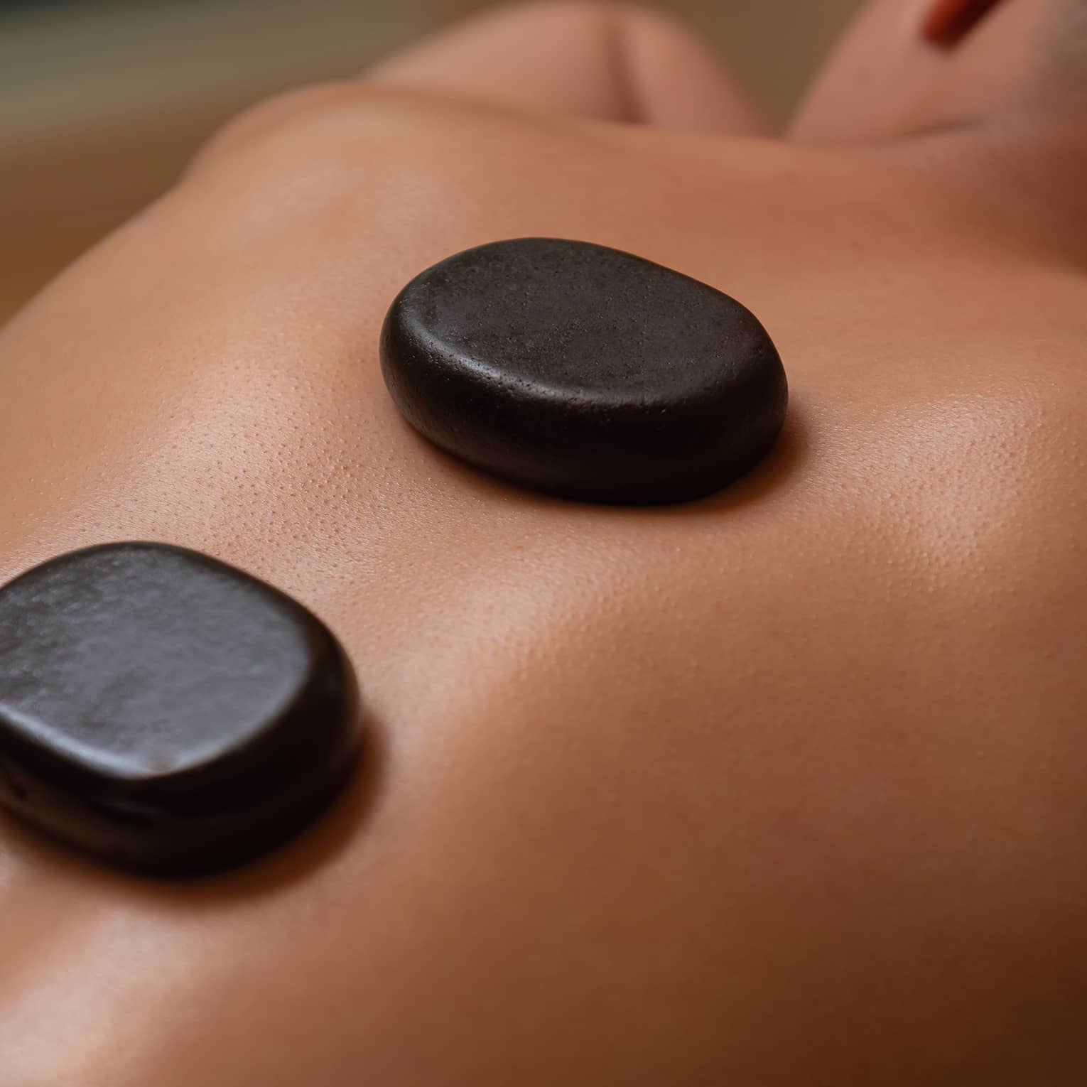 Three large black stones rest on man's bare back and spine as he lays on massage table