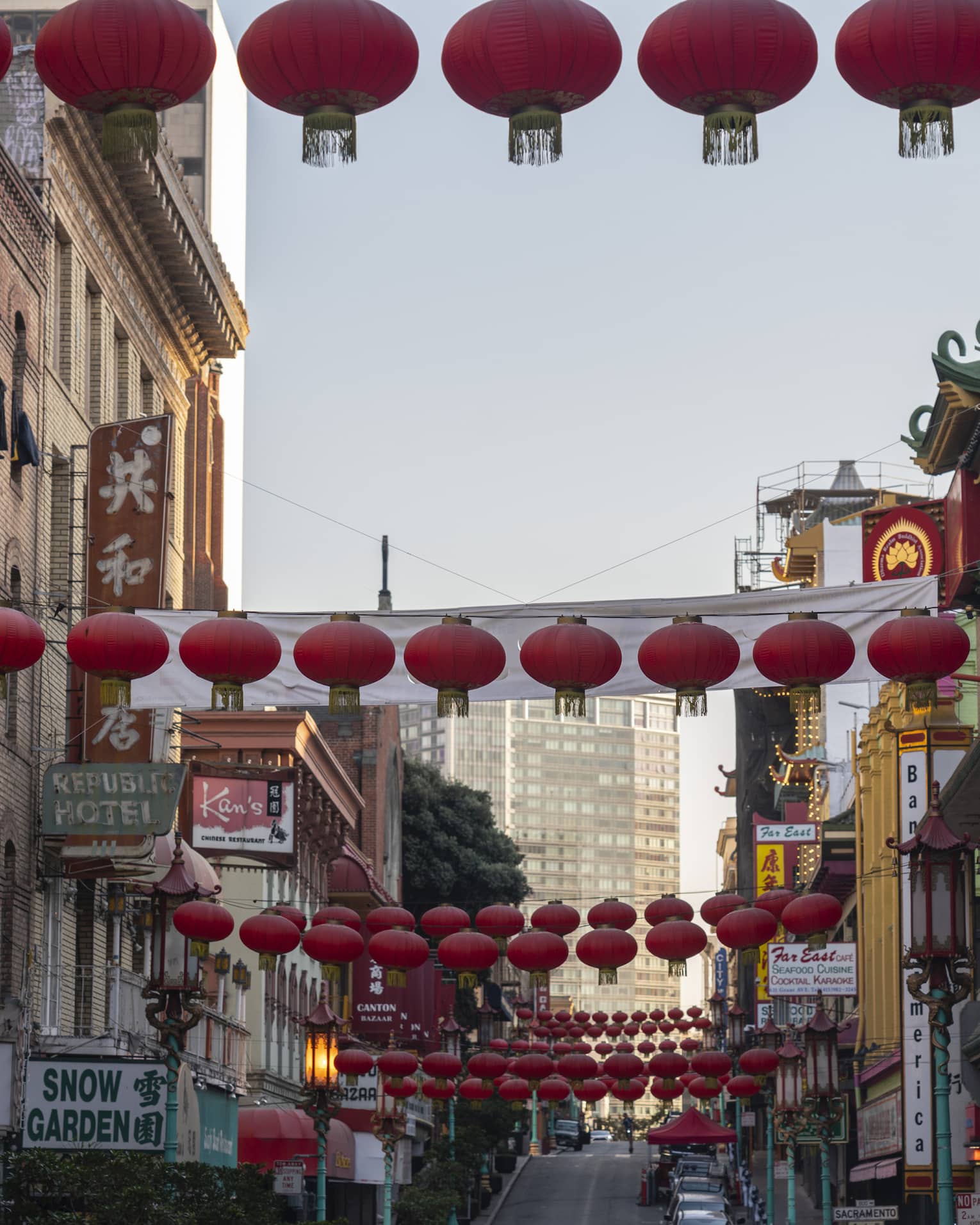 View from the bottom of a Chinatown street lined with restaurants and shops, round red lanterns strung across overhead.