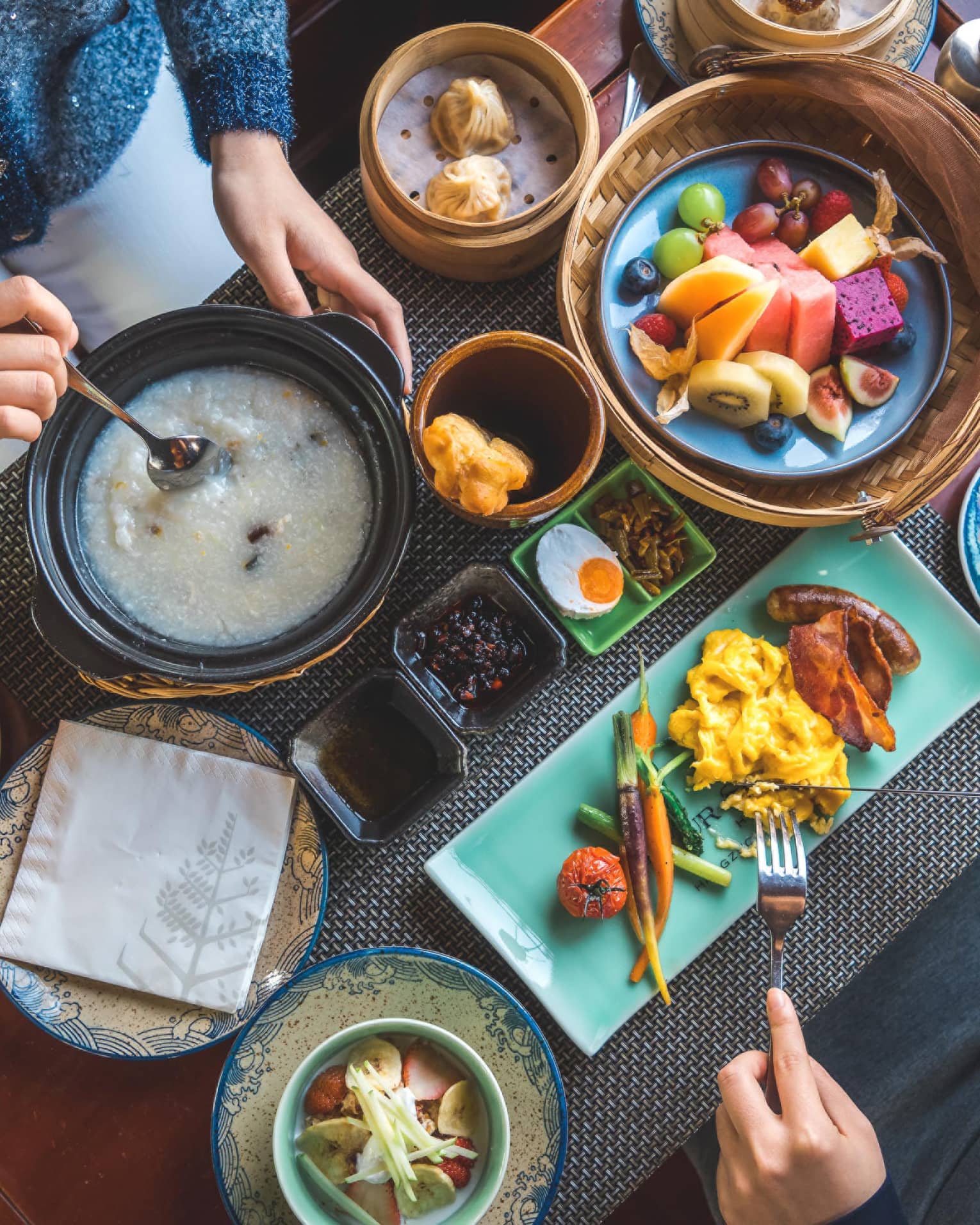 View from above as two guests savour a sumptuous array of vibrant dishes, including pastries, congee, fresh fruit and coffee.