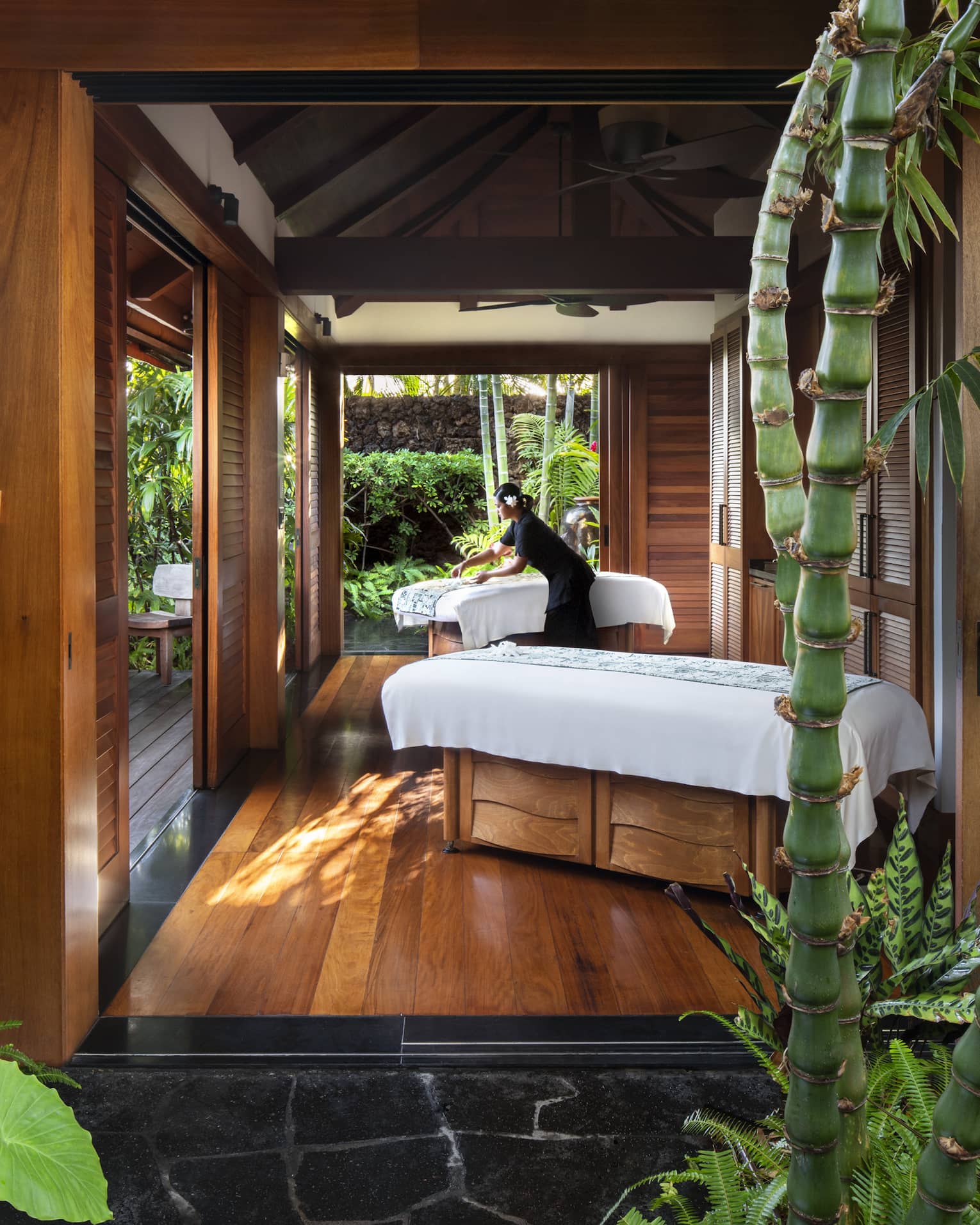 Spa staff spreads sheet on couples massage beds on open-air pavilion