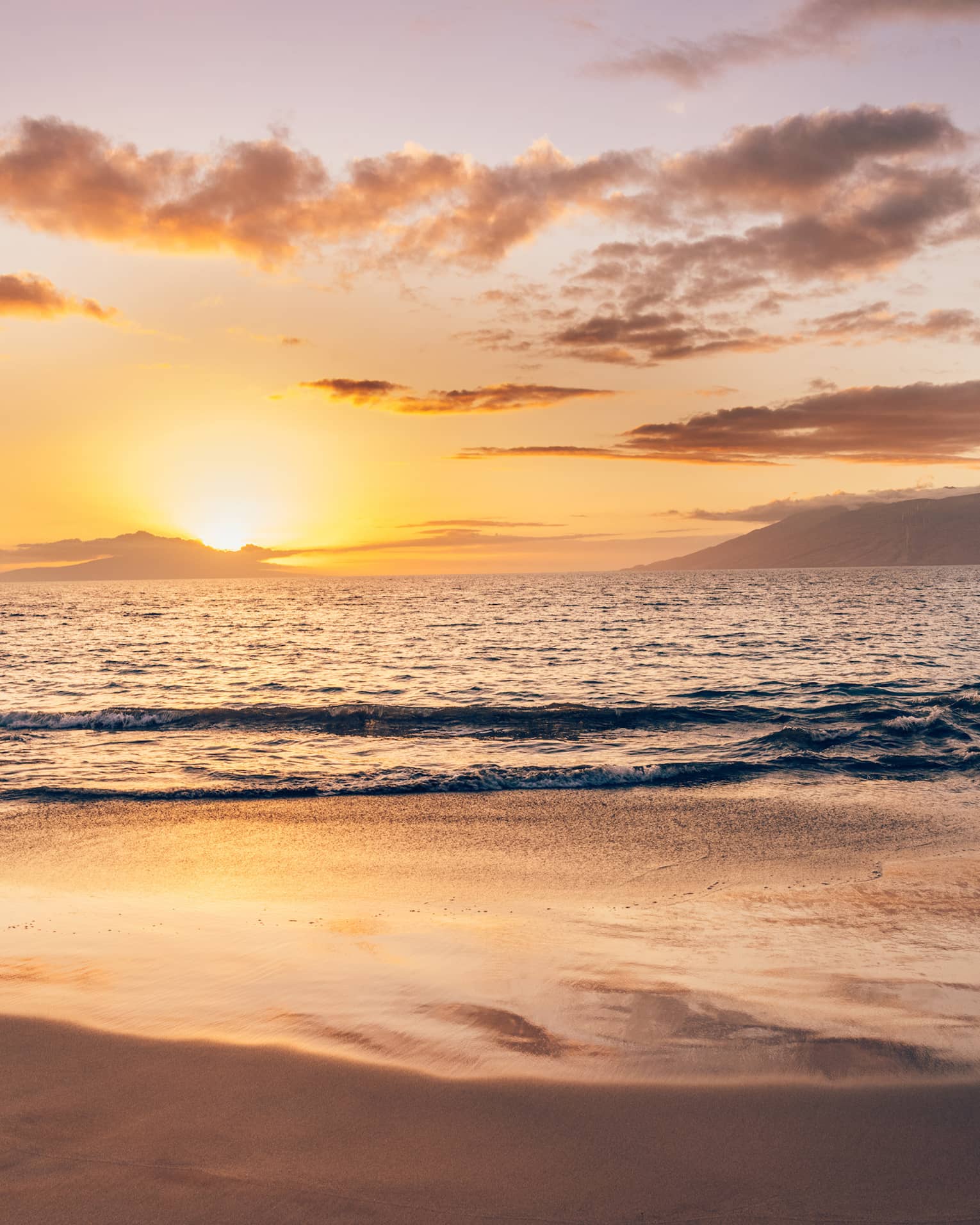Serene beach at sunset with soft waves, golden light reflecting on the sand and clouds over the ocean horizon