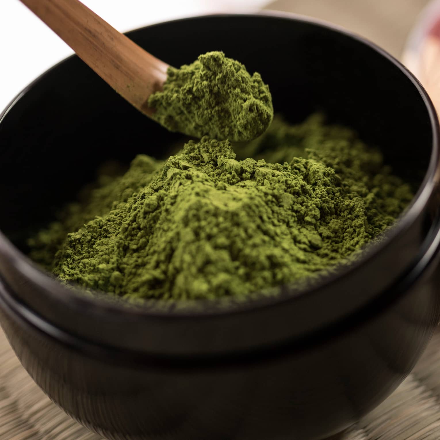 Close-up of green matcha tea powder in small black bowl, wood spoon