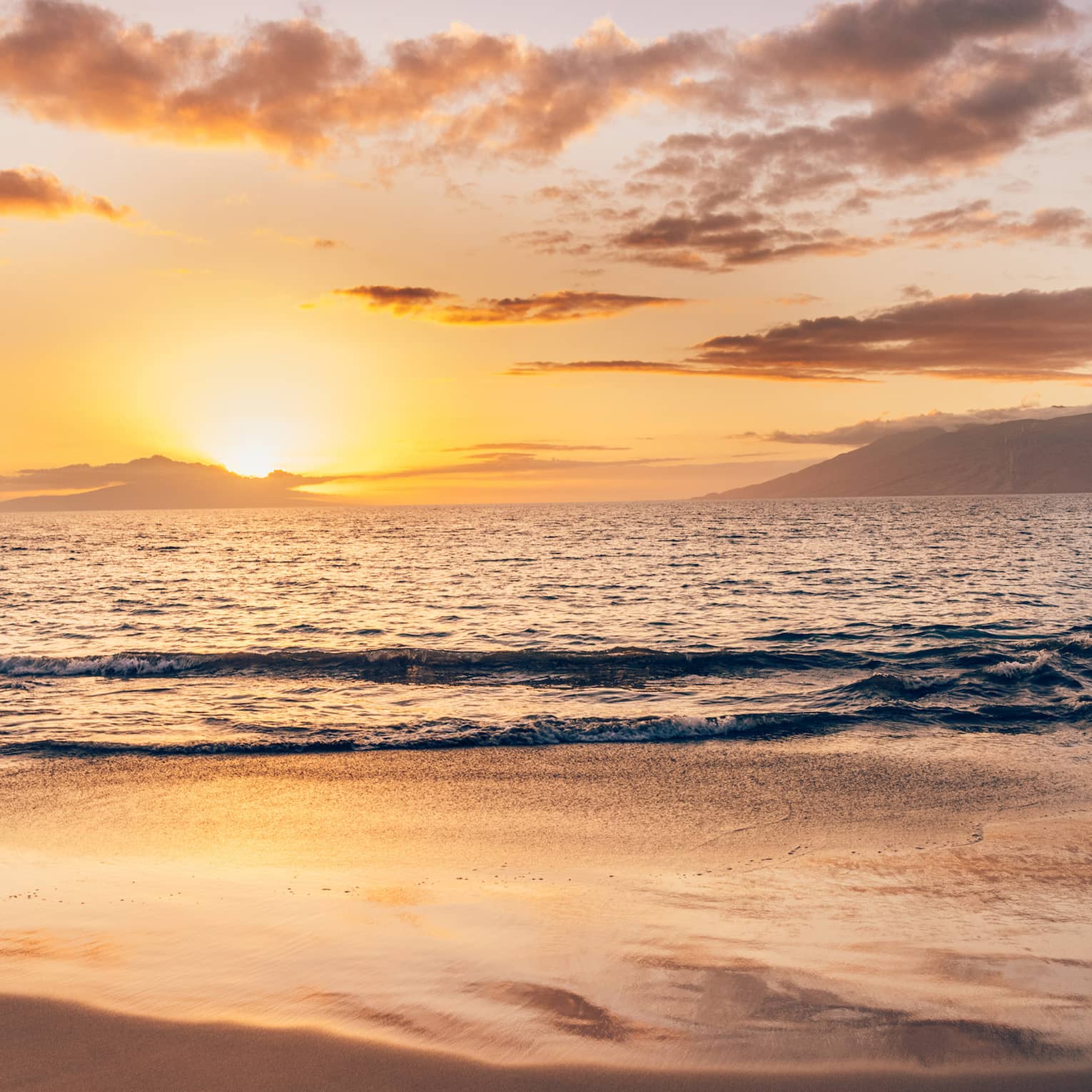 Serene beach at sunset with soft waves, golden light reflecting on the sand and clouds over the ocean horizon